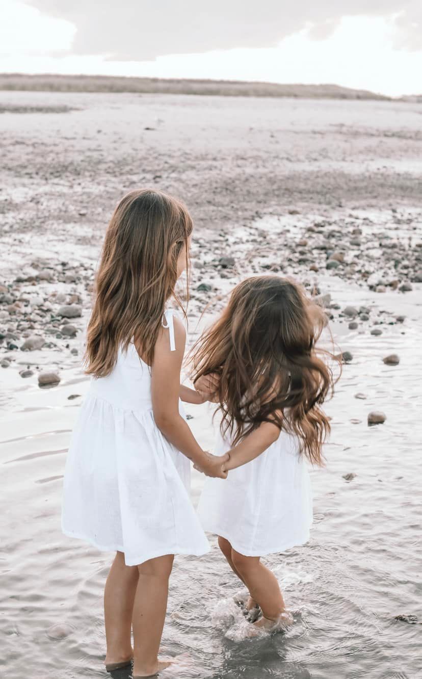 Two children in white dresses playing at the beach edge.