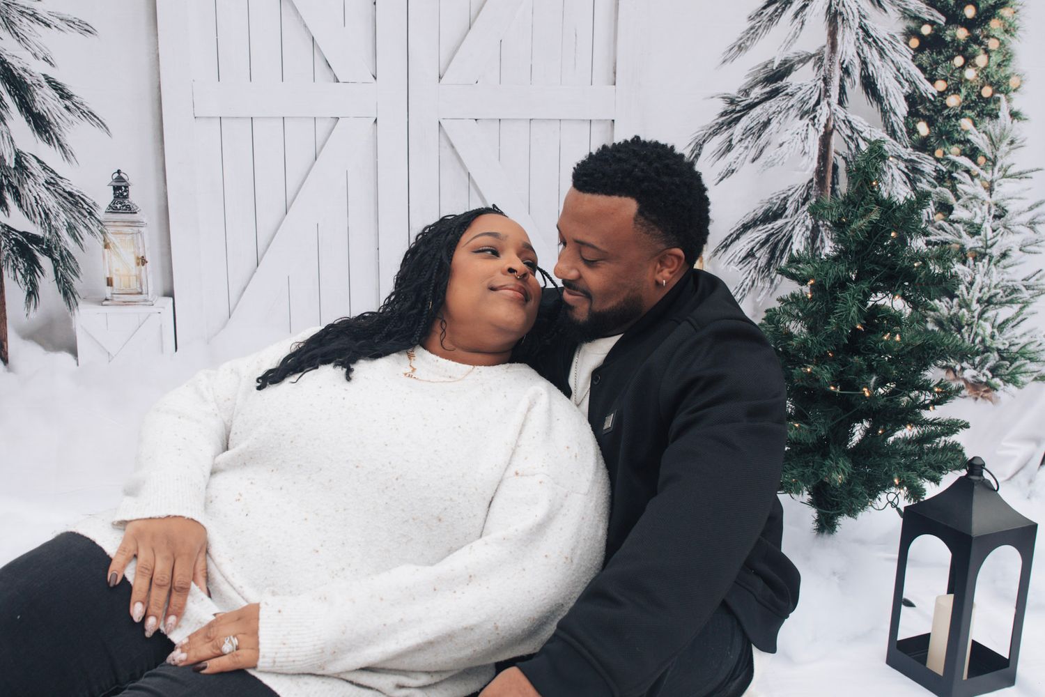 Couple sharing intimate moments in a winter photoshoot with snow and white barn background.