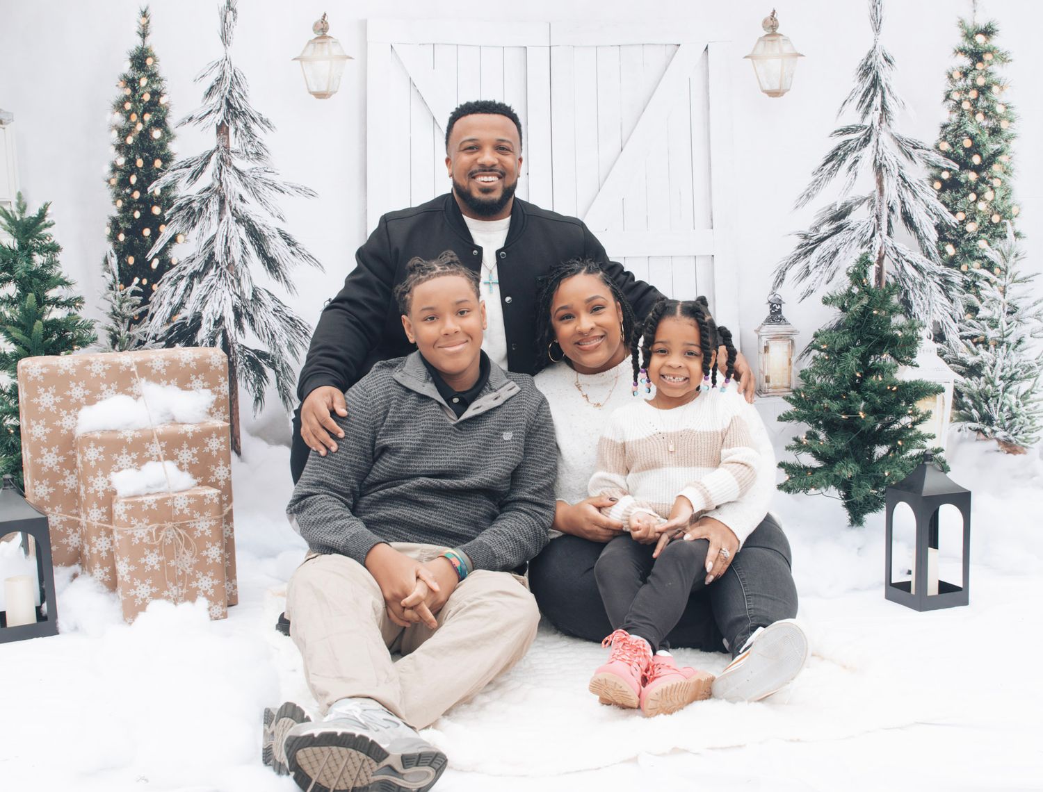 Family sitting together in winter outfits against a white barn backdrop with snow and evergreens.