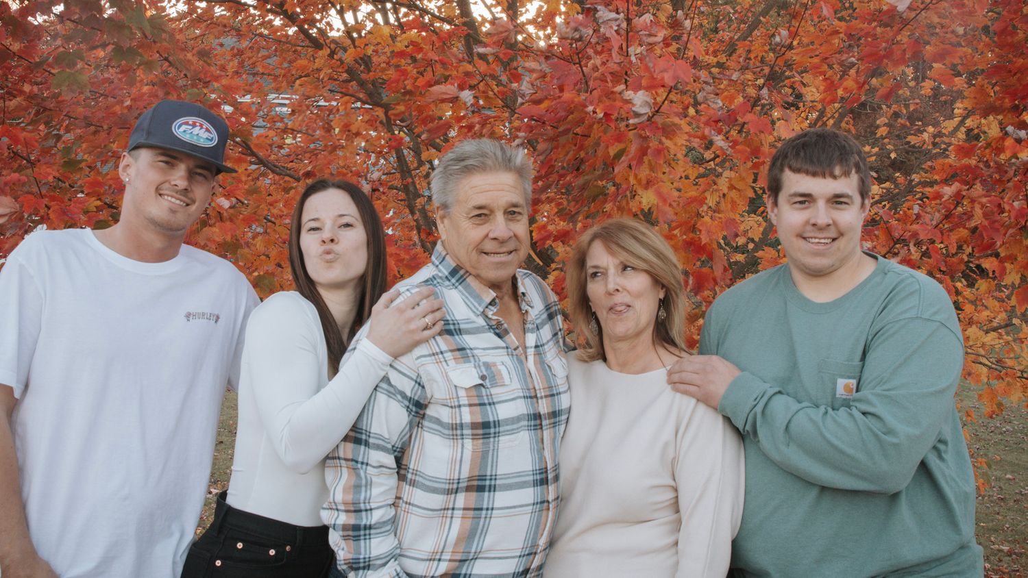 A group of people pose together in front of vibrant orange autumn foliage.