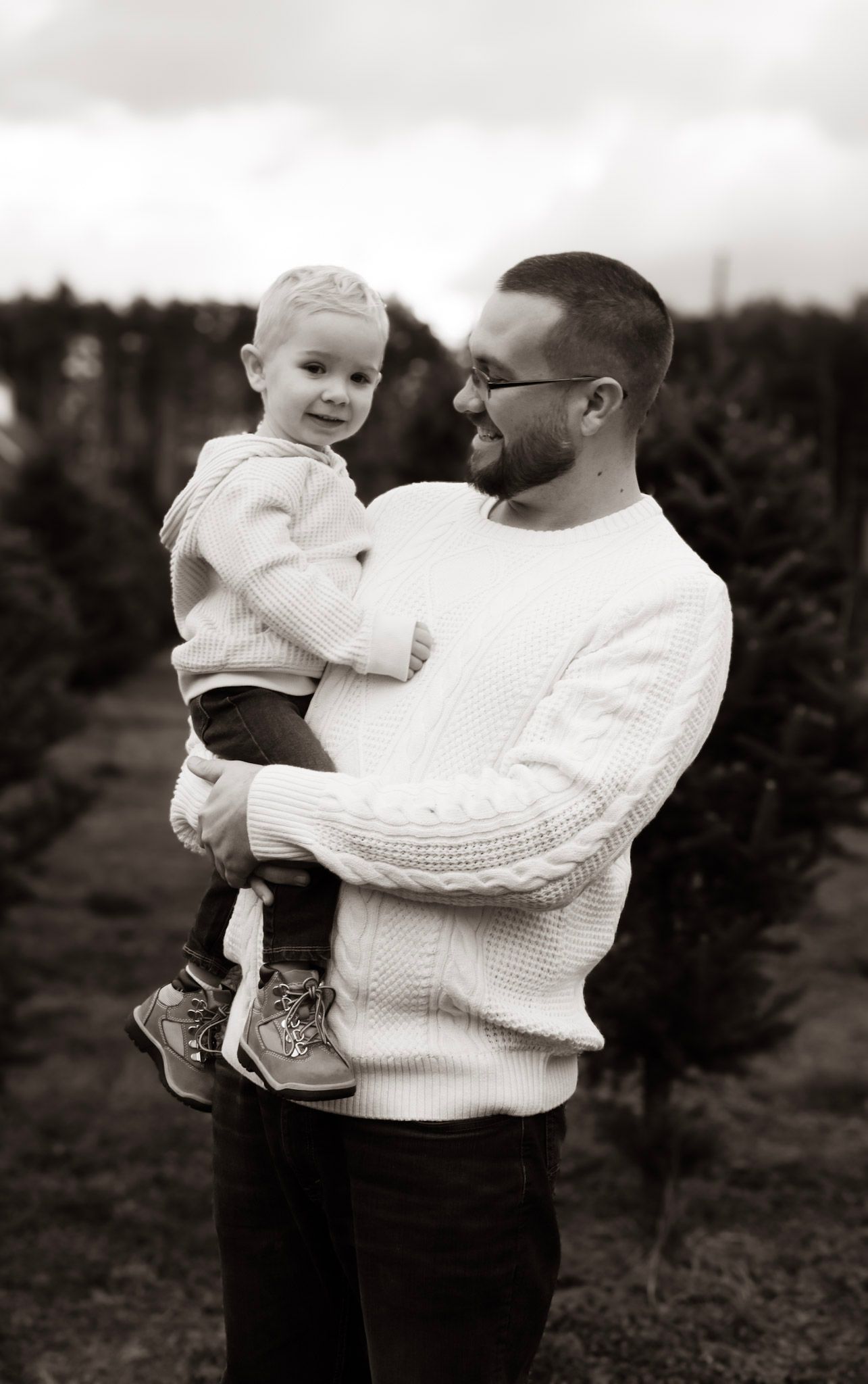 A tender black and white photo series showing a parent in a white sweater holding and interacting with a baby outdoors.