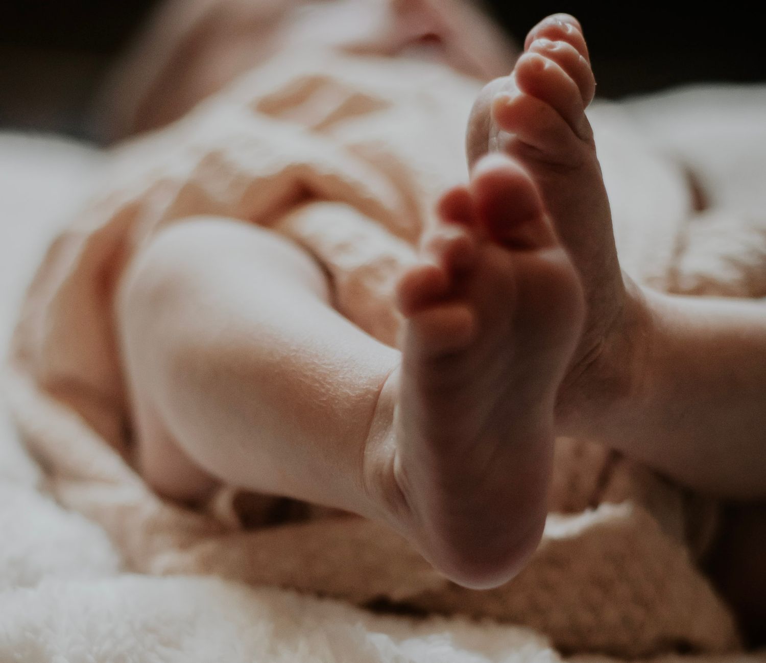 Close-up view of tiny newborn baby toes and feet against a soft white background.