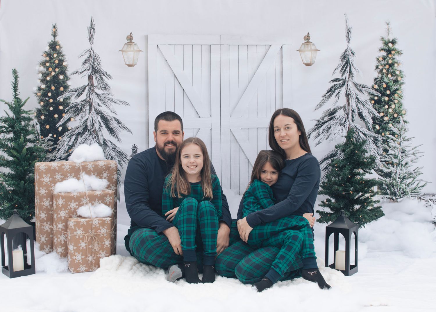 Winter family photo session with snow-covered trees and white barn doors in background.