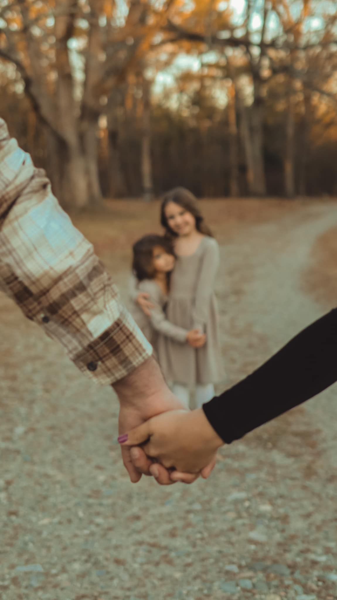 Couple holding hands while walking through fallen autumn leaves in a park.