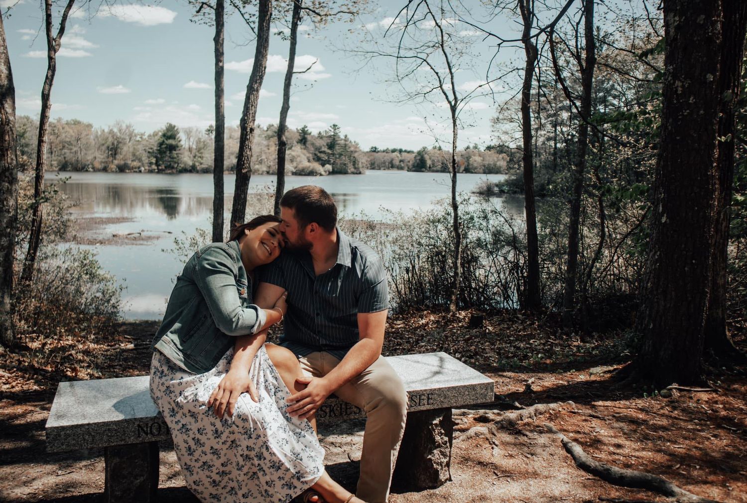 Couple sharing an intimate moment on a bench by a serene lake surrounded by trees.