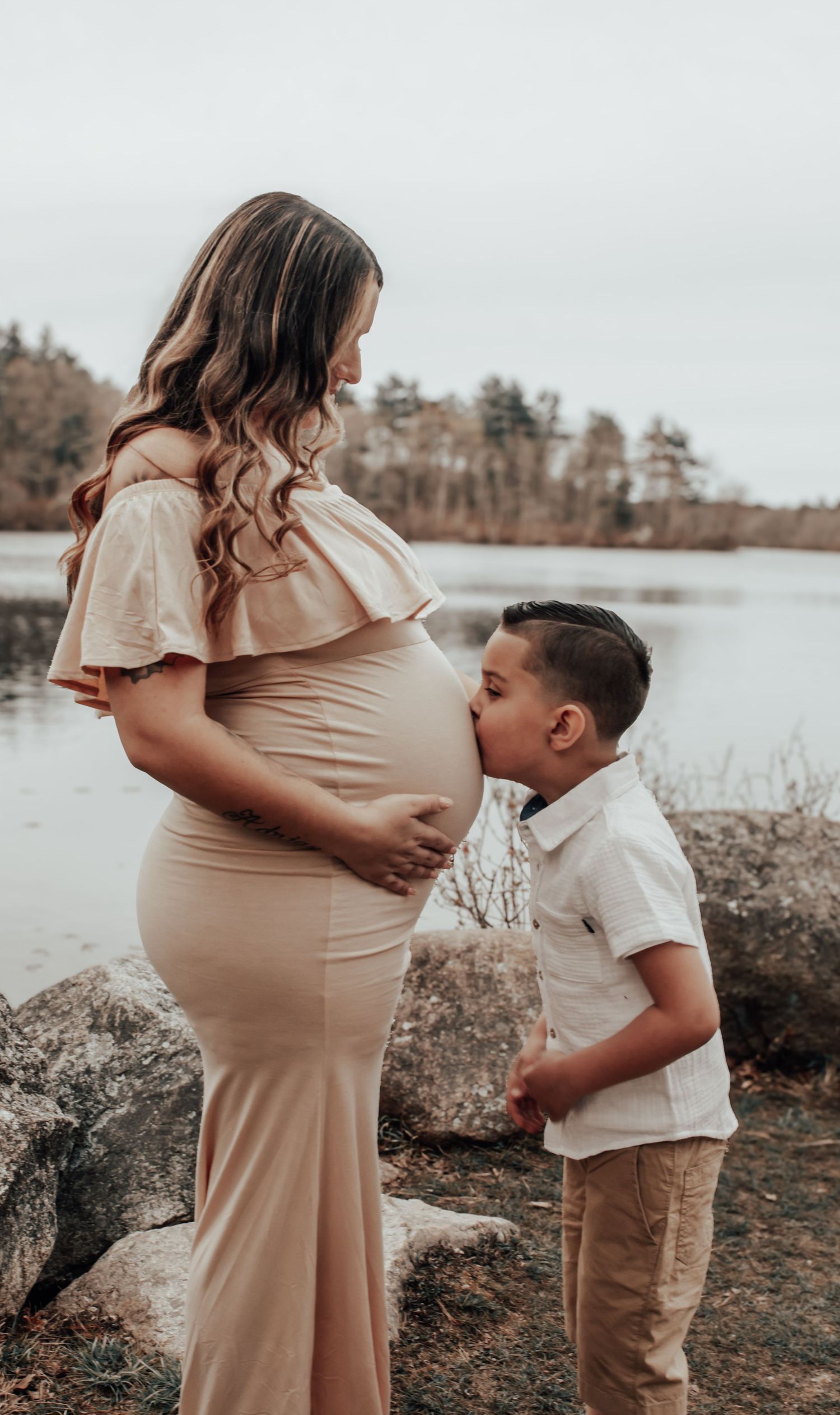 Tender moment between mother and child during lakeside maternity photoshoot.