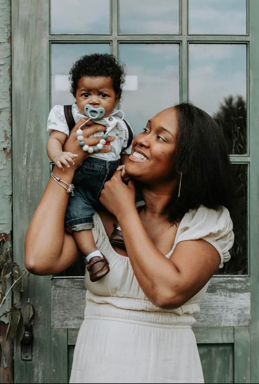A parent and baby share playful moments in front of a rustic window.