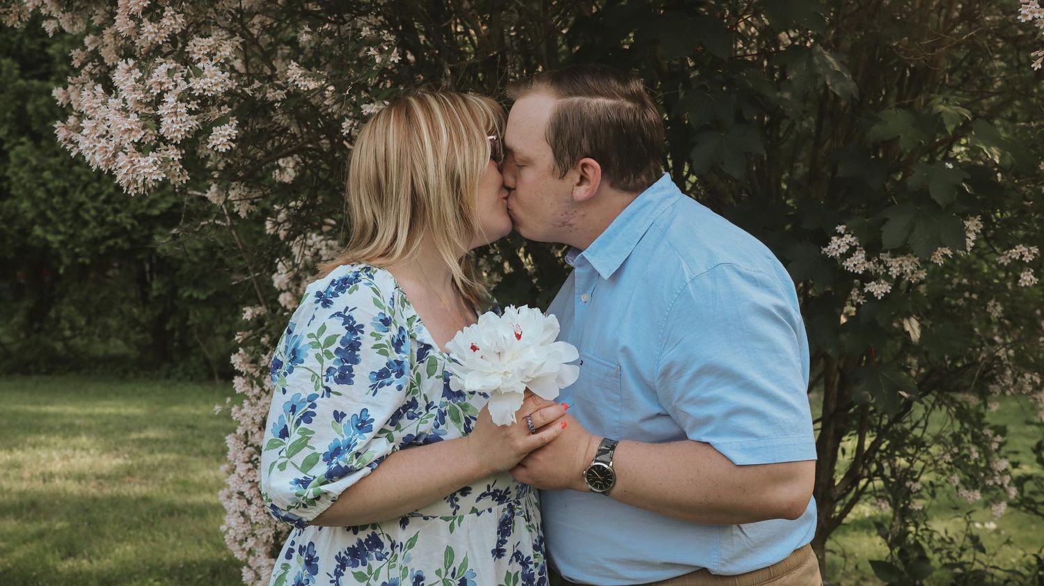 Couple sharing a tender kiss in a garden setting with blooming flowers in the background.