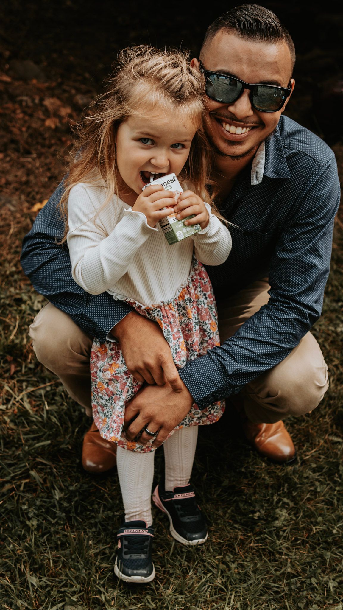 A heartwarming outdoor moment captured in warm lighting with a floral dress and sunglasses.