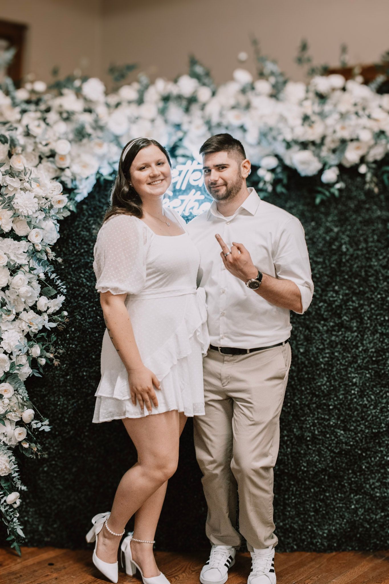 Family gathering in front of white floral wall with people dressed in white and beige outfits.