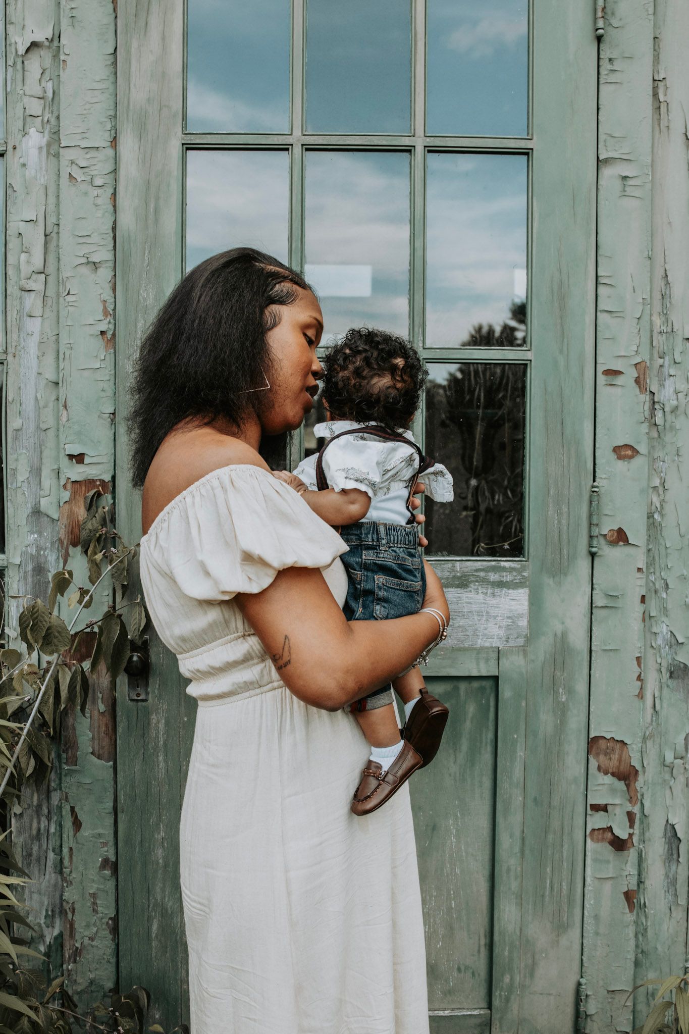 A mother in a white dress holds and kisses her baby against a weathered mint green door in a multi-panel photo series.