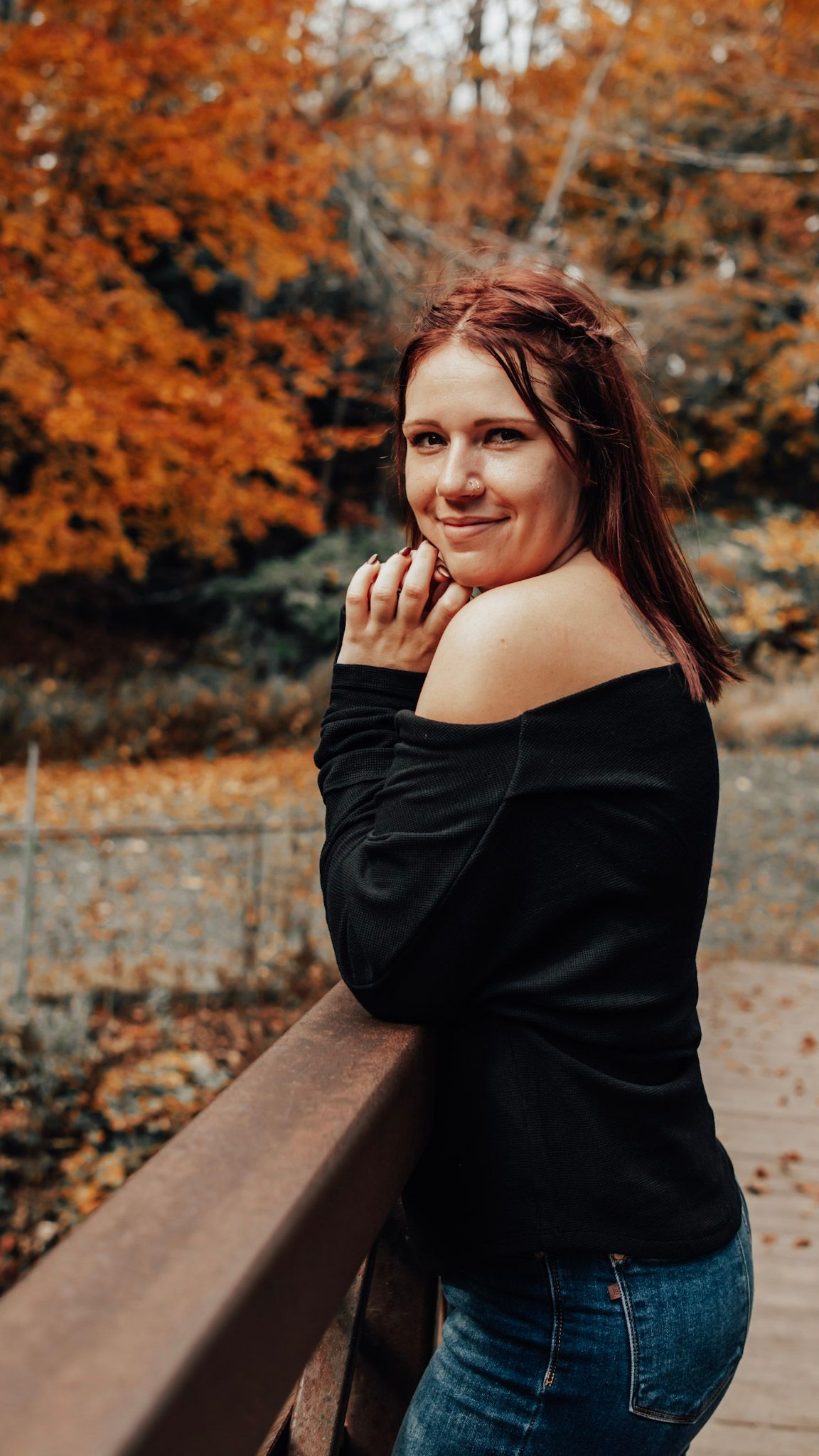 Autumn portrait series with person in black sweater and jeans against vibrant orange fall foliage.
