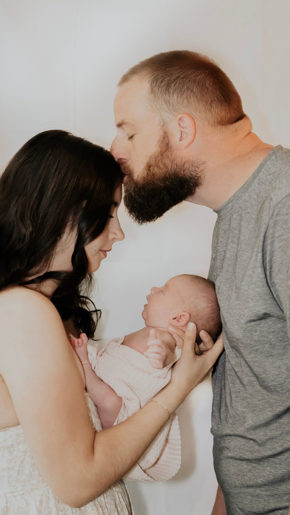 An intimate family portrait showing parents cradling their newborn baby while sharing a loving moment together.