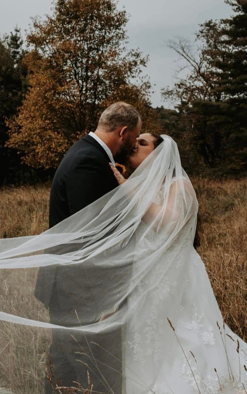 Dramatic wedding photo with flowing veil in an autumn field with golden foliage.