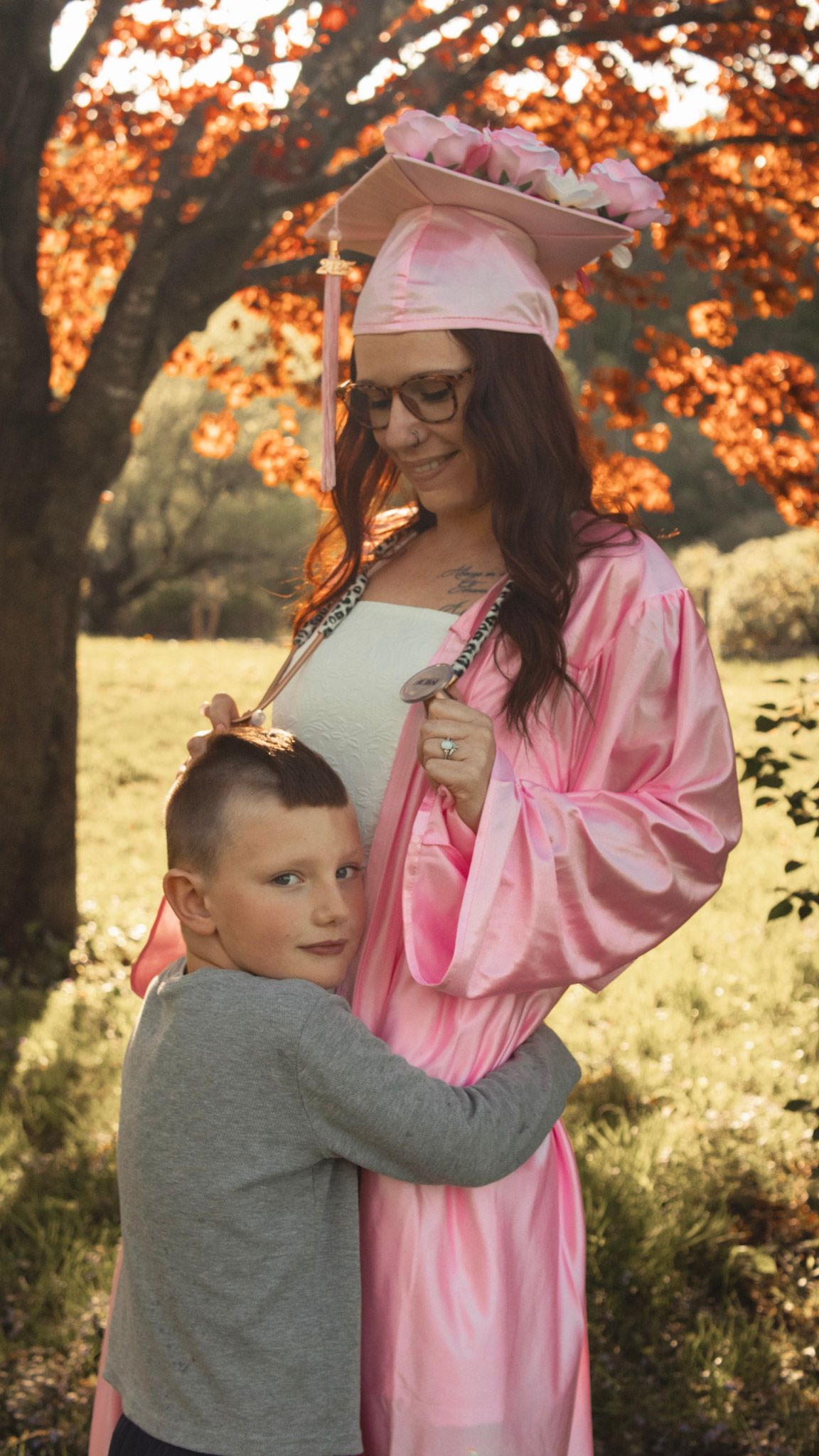 Autumn scene with person in pink dress and child in grey sharing a tender moment.
