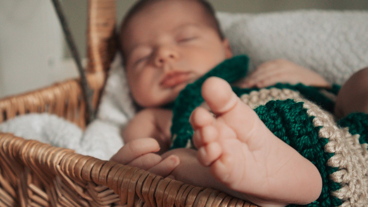 A baby sleeps peacefully on a soft white blanket while wearing a green knitted outfit.