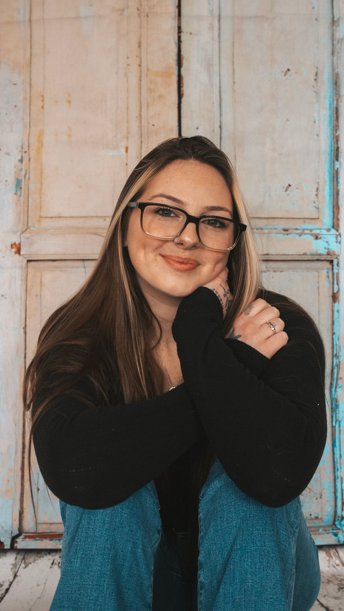 A collage of three similar poses showing someone wearing glasses and a teal and black outfit against a rustic wall.
