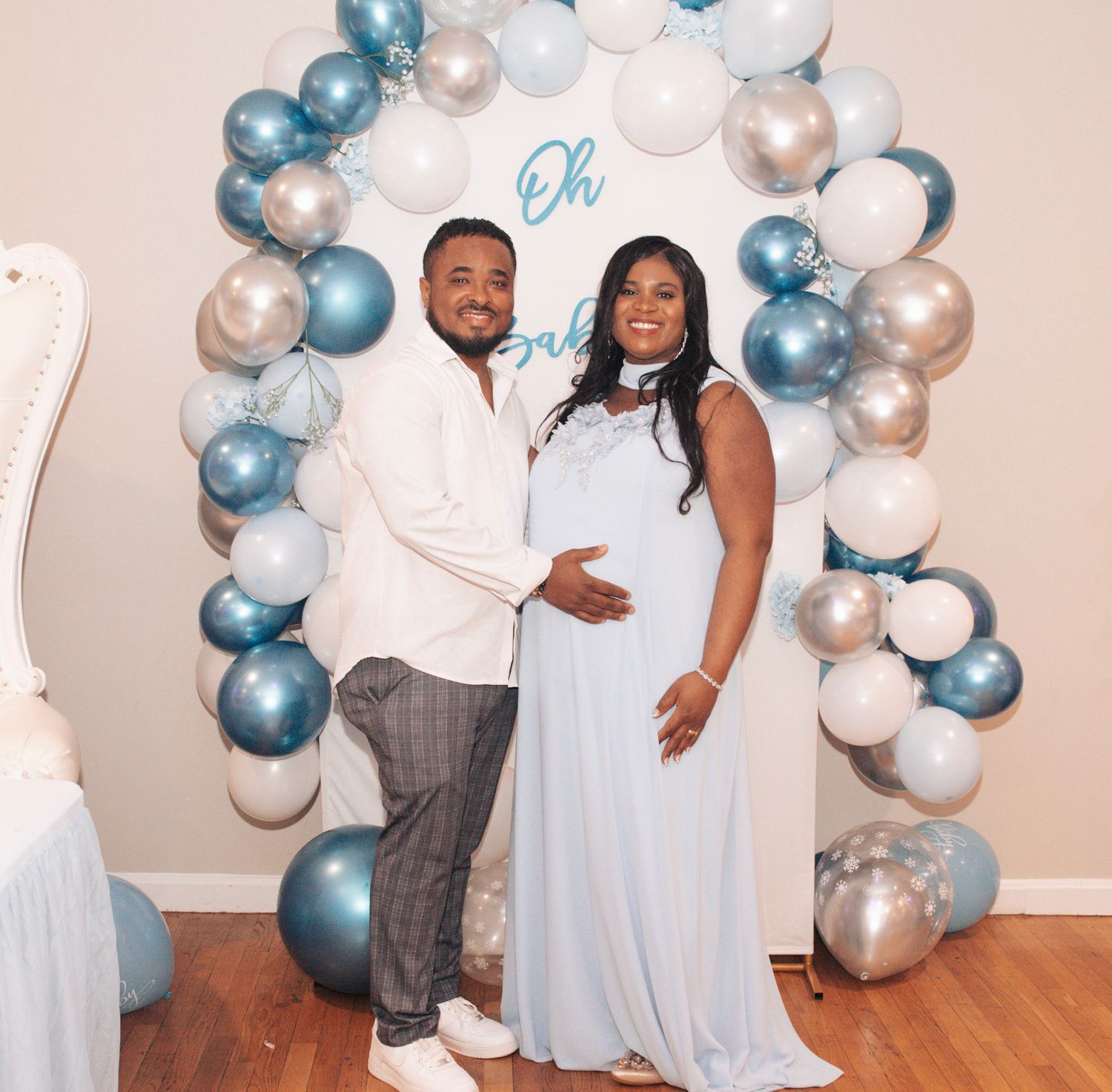 Baby shower celebration with blue and white balloon arch decorations against a light colored wall.