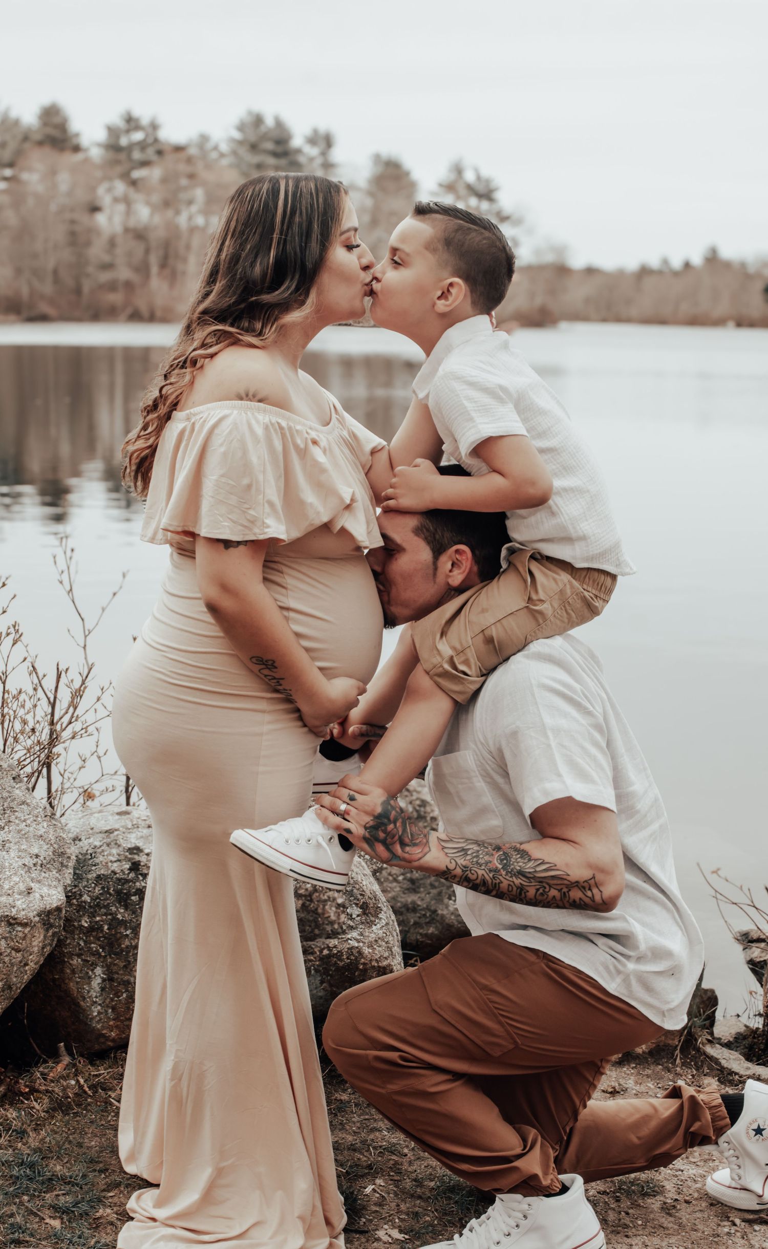 Family maternity photo session by a serene lakeside in muted tones.