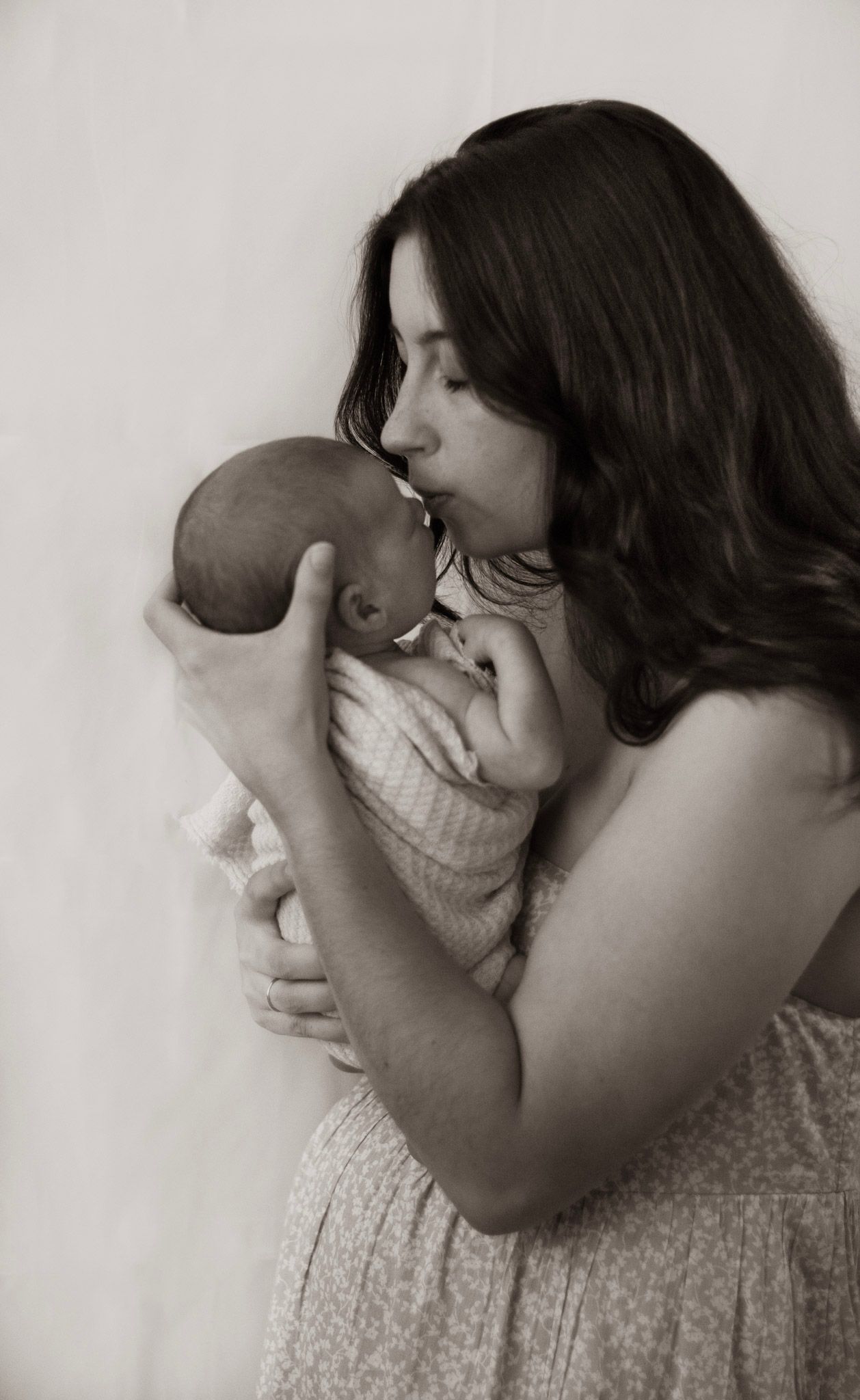 A series of black and white photos showing a tender moment between a mother and infant in soft, gentle lighting.