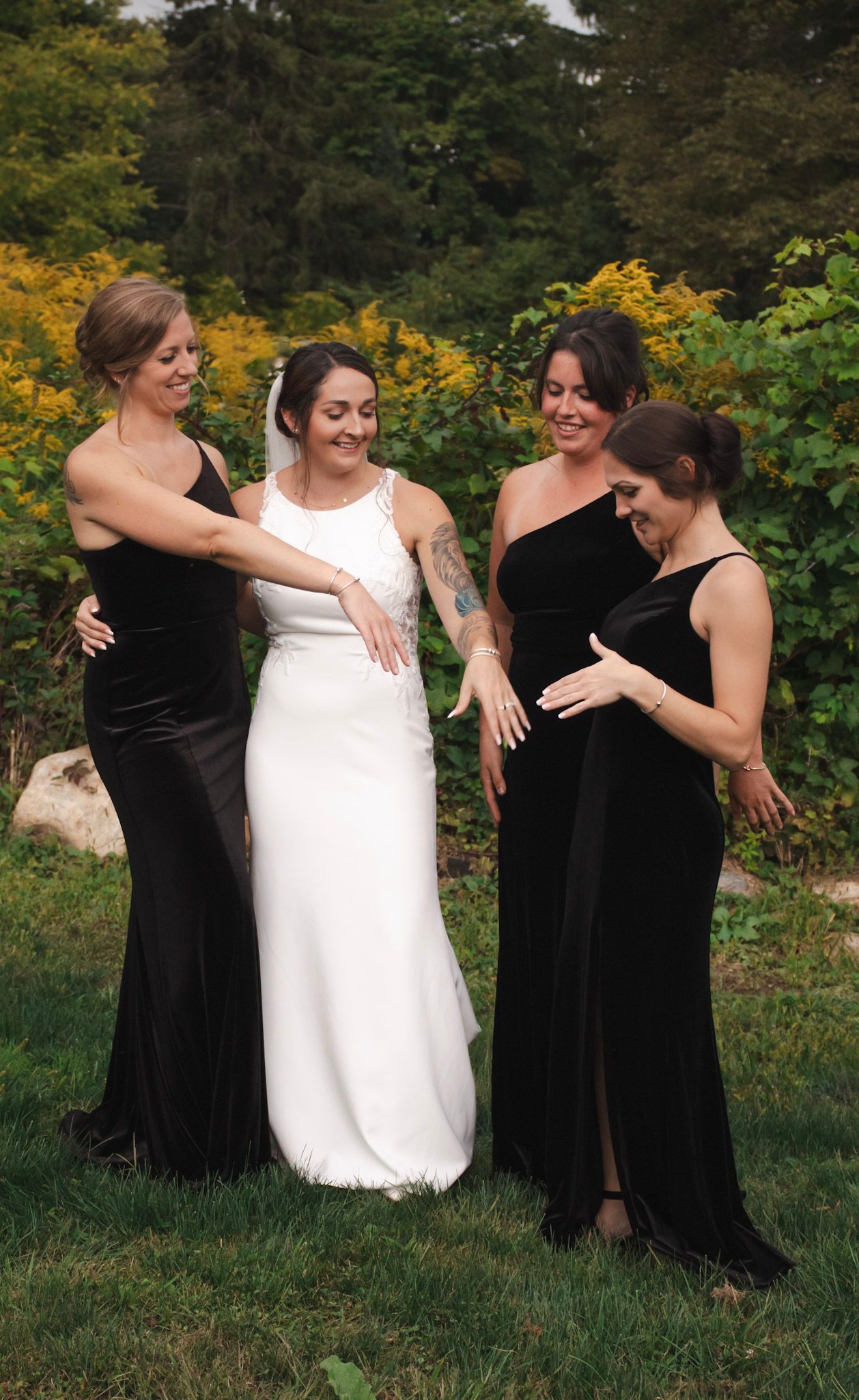A group wearing black and white dresses share joyful moments while posing together outdoors in a garden setting.