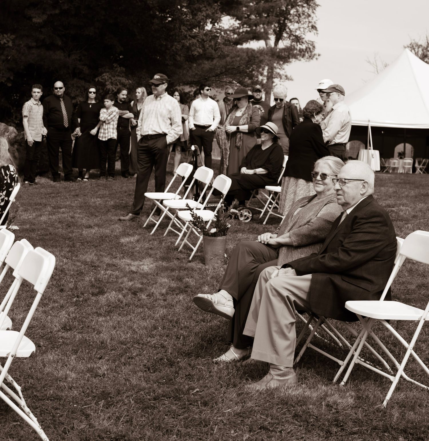 Vintage panoramic photograph showing people seated in white folding chairs on a grassy lawn at an outdoor gathering.