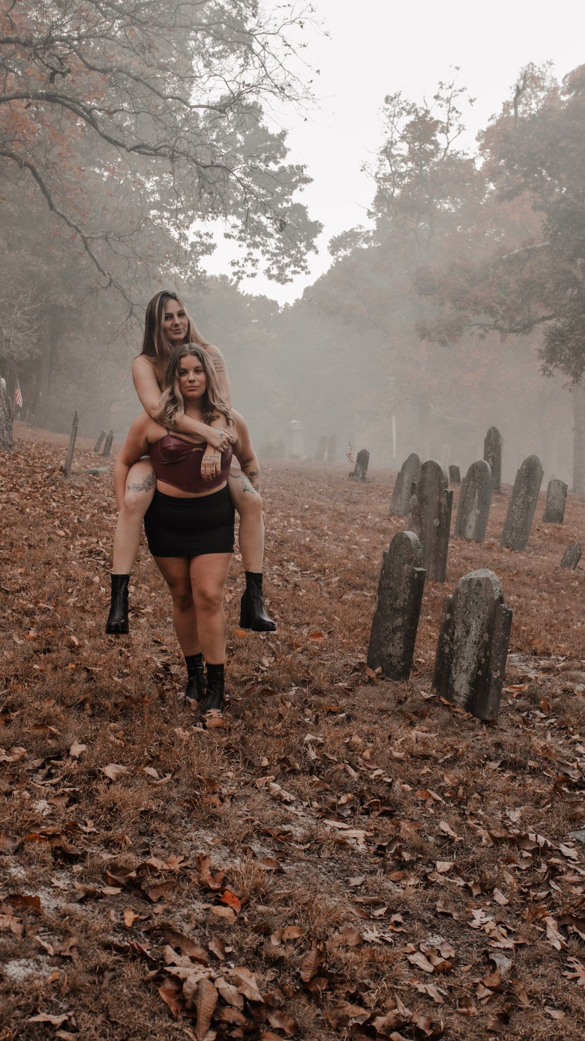 A person in dark athletic wear crouches among fallen autumn leaves in a foggy cemetery with old headstones.