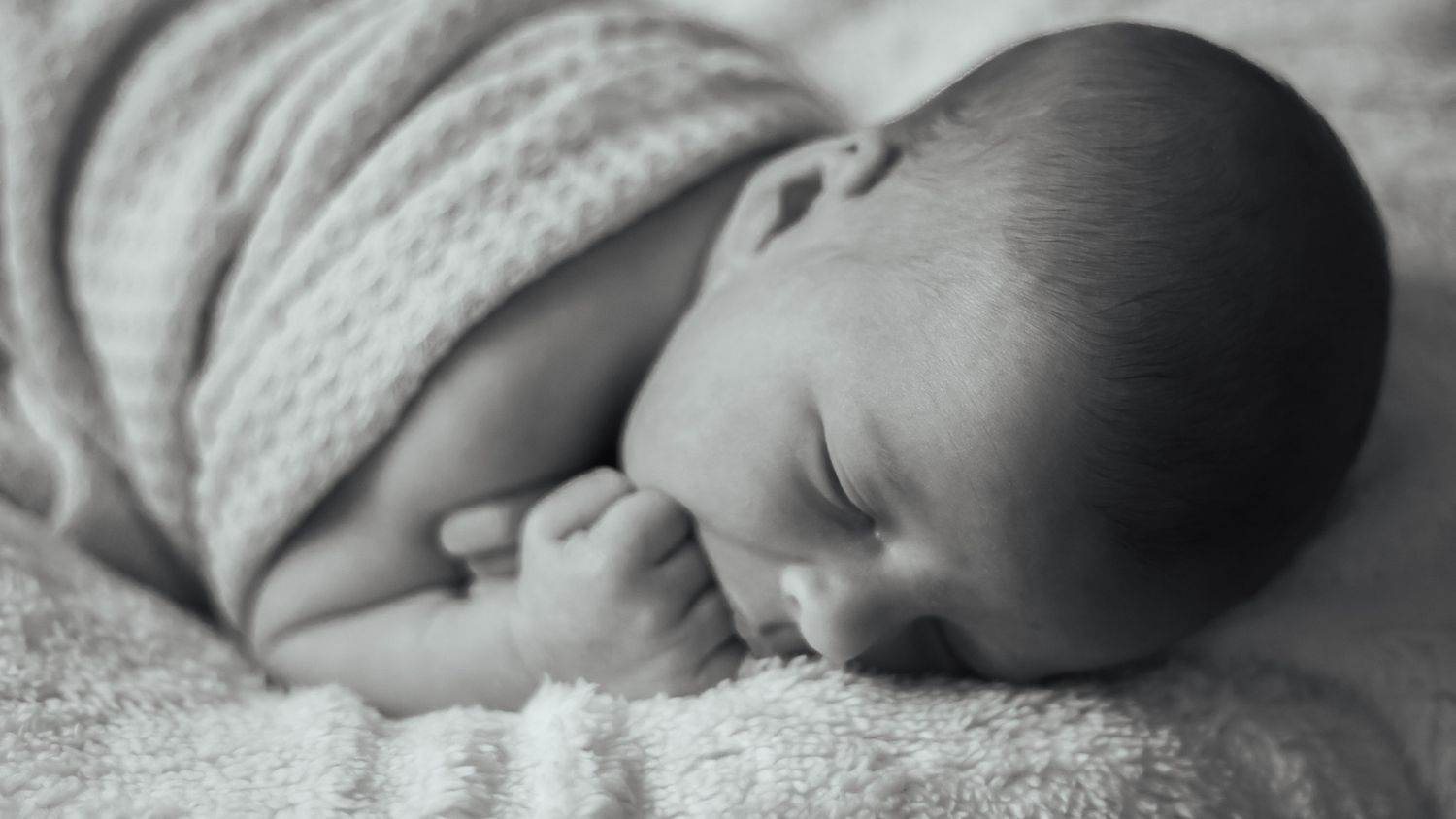 Peaceful sleeping newborn photographed in black and white on textured knit blanket.