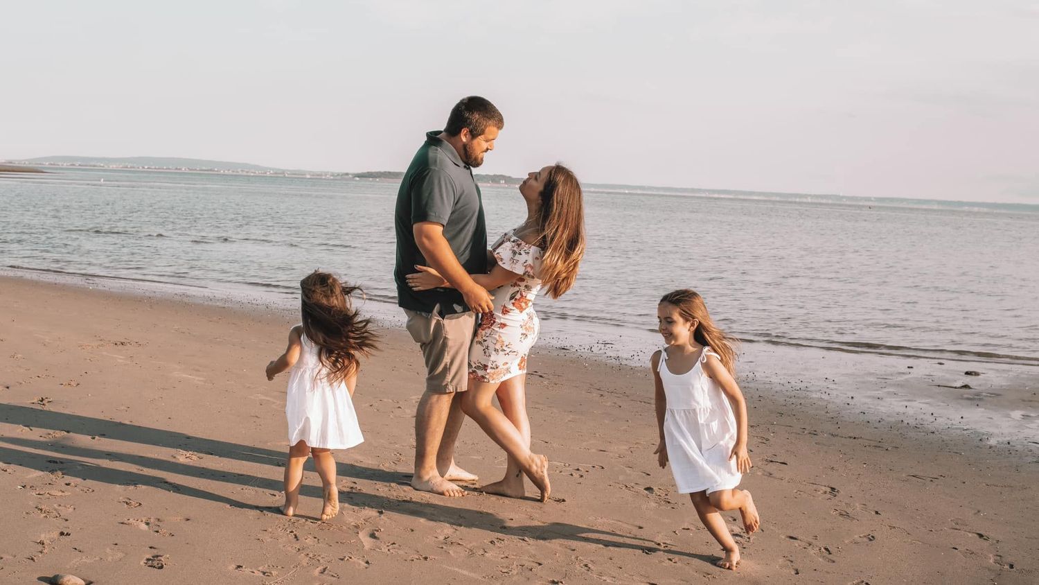 Family enjoying a playful moment together on sandy beach at sunset.
