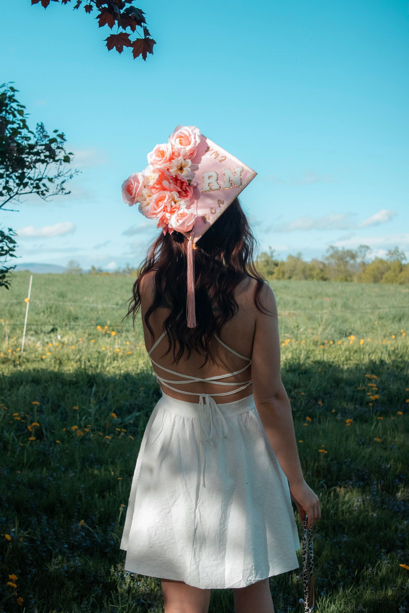 White dress and pink bonnet captured against blue sky in meadow setting.