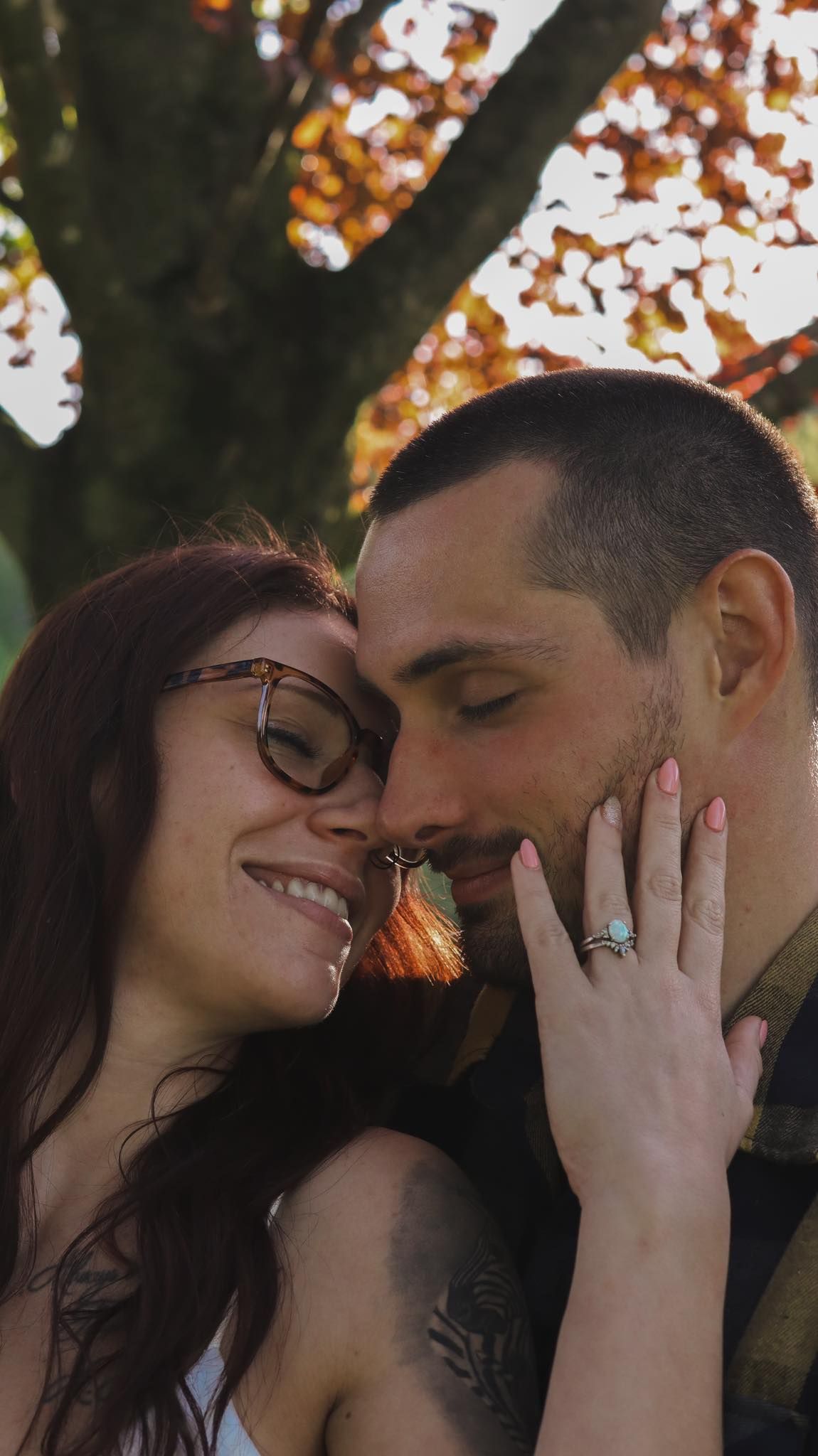 Intimate couple shares tender moments under autumn trees during engagement photoshoot.