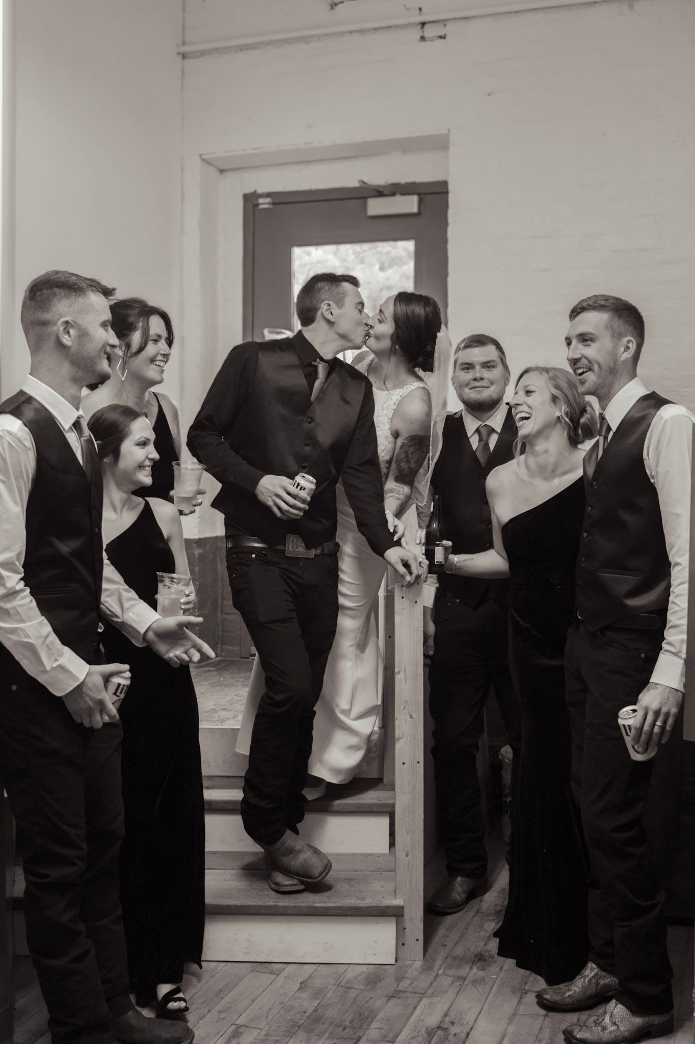 A group of formally dressed dancers share laughs while practicing in a mirrored studio space.
