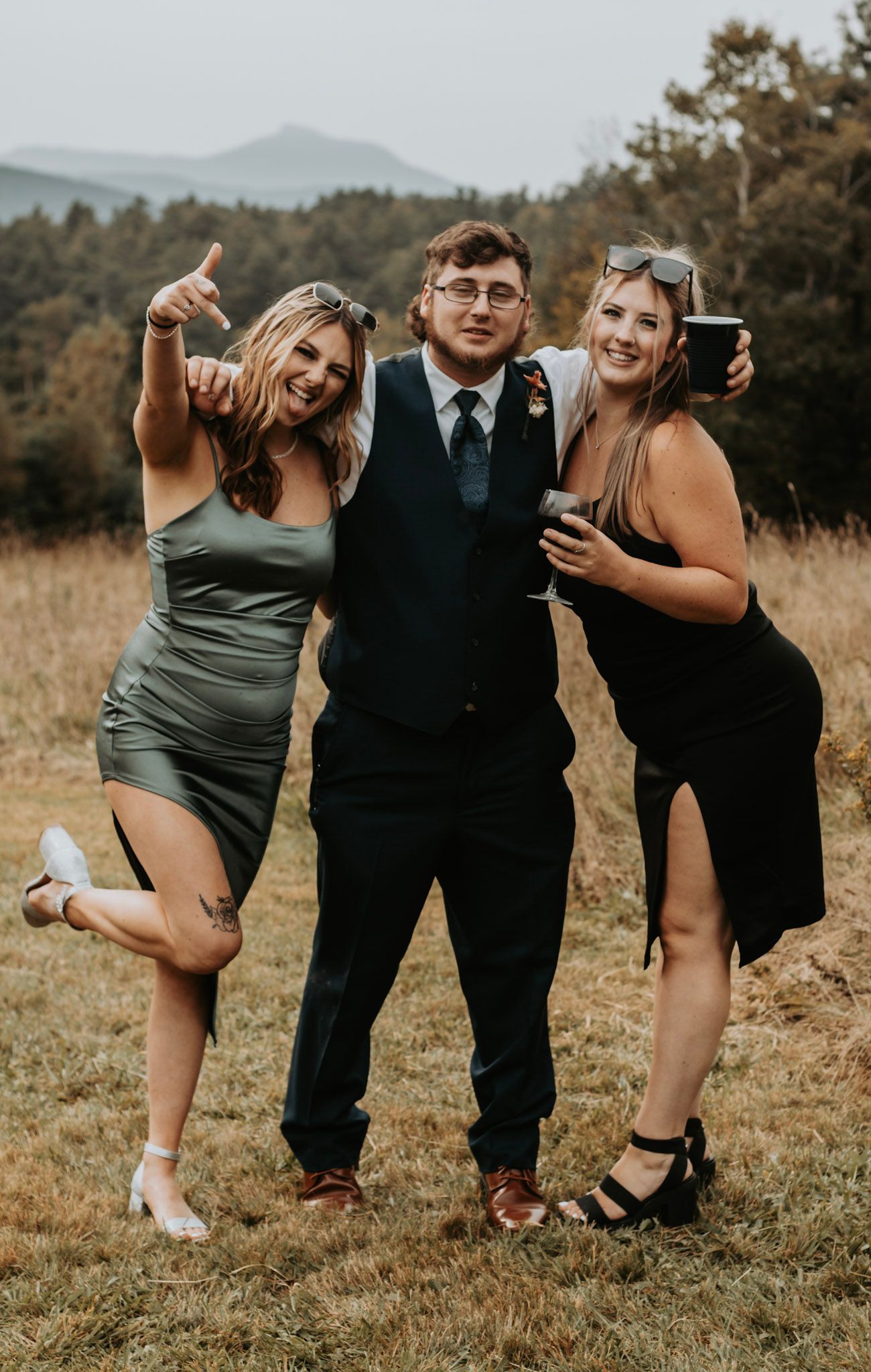 Three friends pose playfully in formal attire against a mountainous autumn landscape at golden hour.