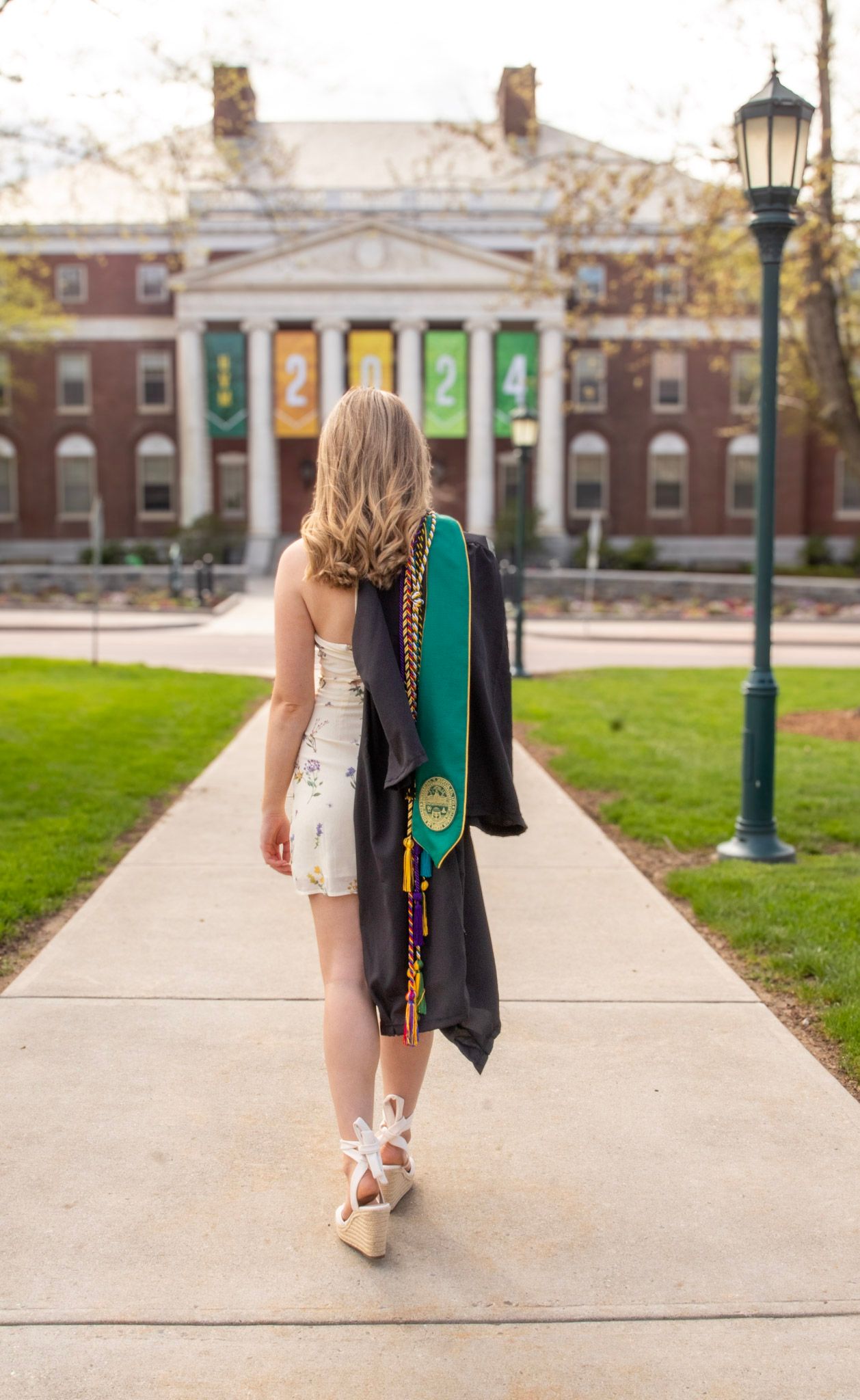 Green graduation stoles with tassels swaying against a collegiate campus backdrop with brick buildings.