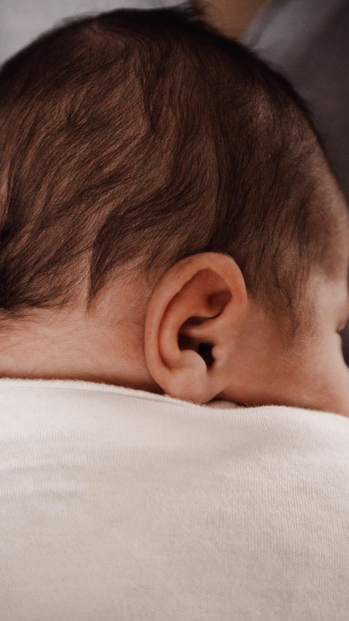 Detail shot of a sleeping baby's head resting against white fabric.