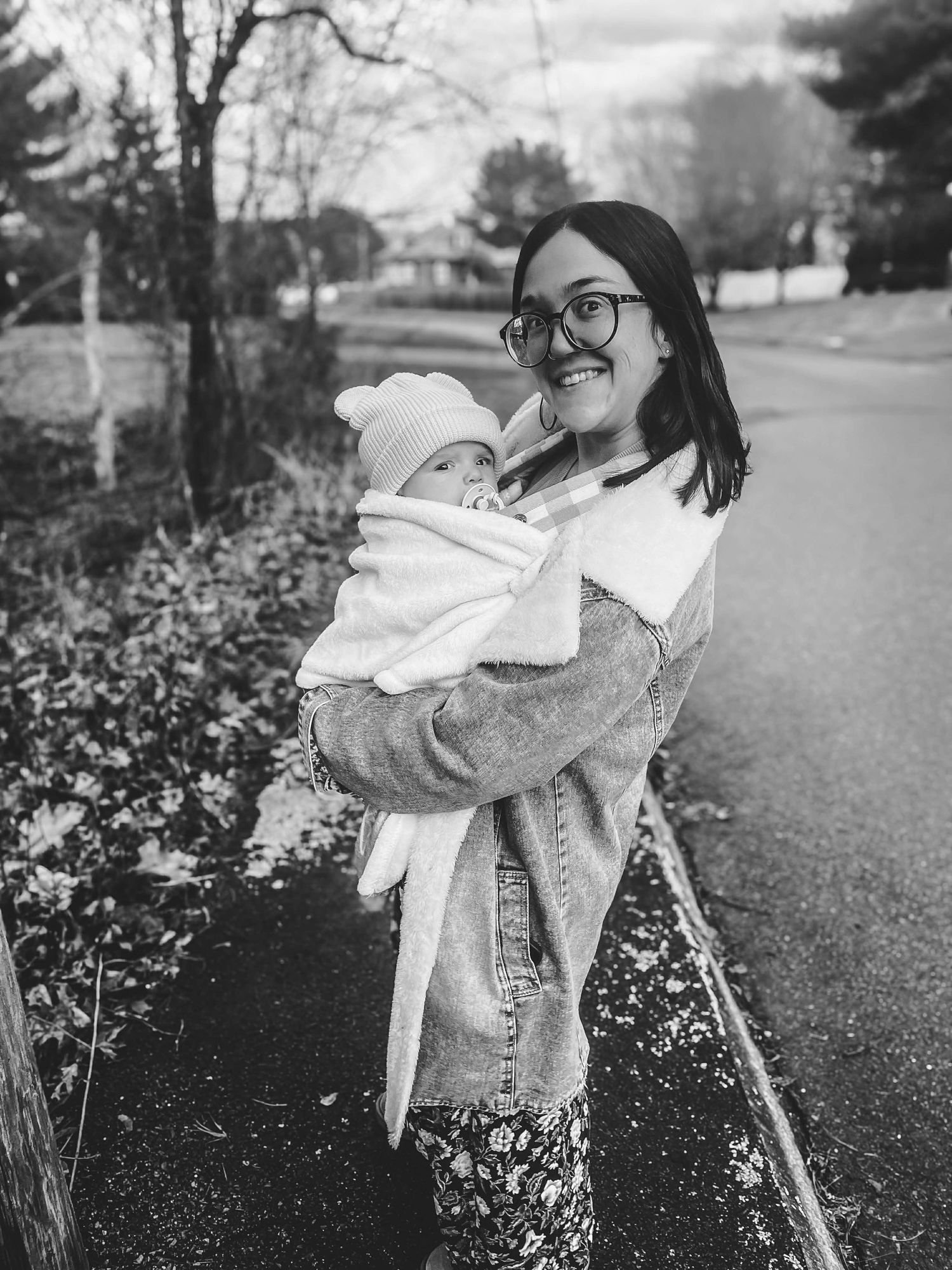 Black and white photo of parent cradling infant outdoors on residential street.