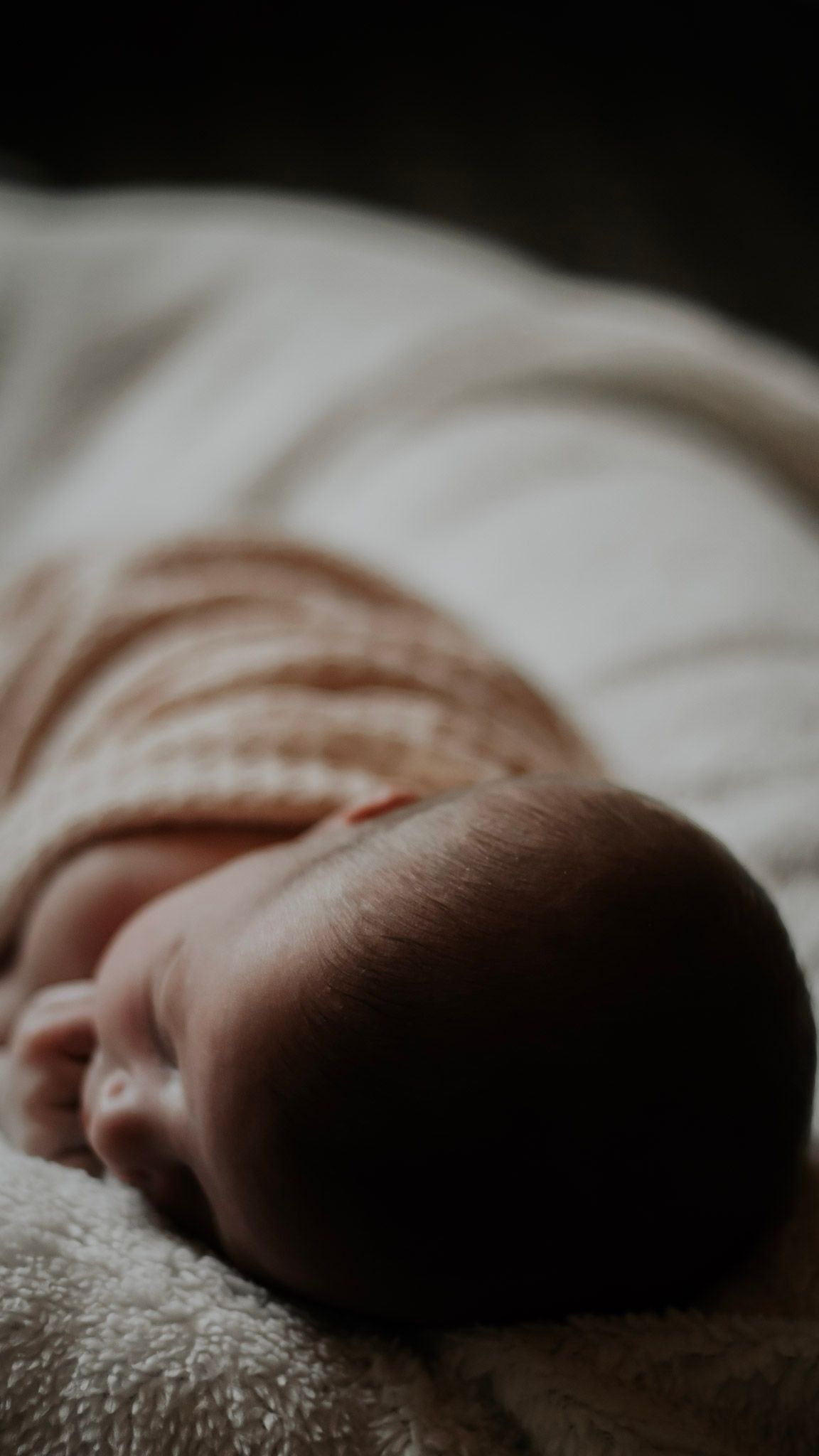 Close-up macro shot of a sleeping baby's profile against soft white bedding in natural light.