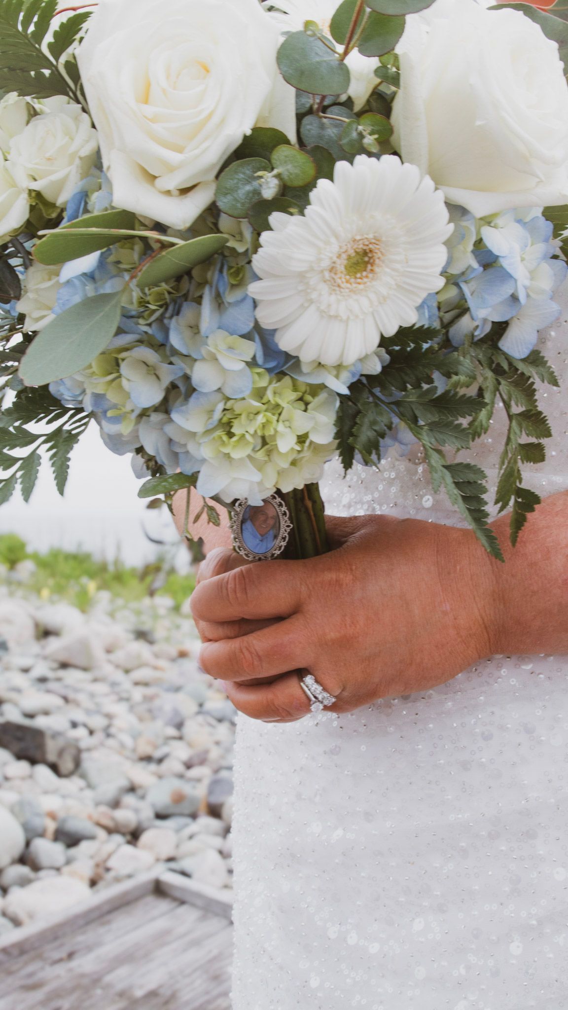 A delicate bridal bouquet of white roses, blue hydrangeas and eucalyptus leaves is held against a snowy backdrop.