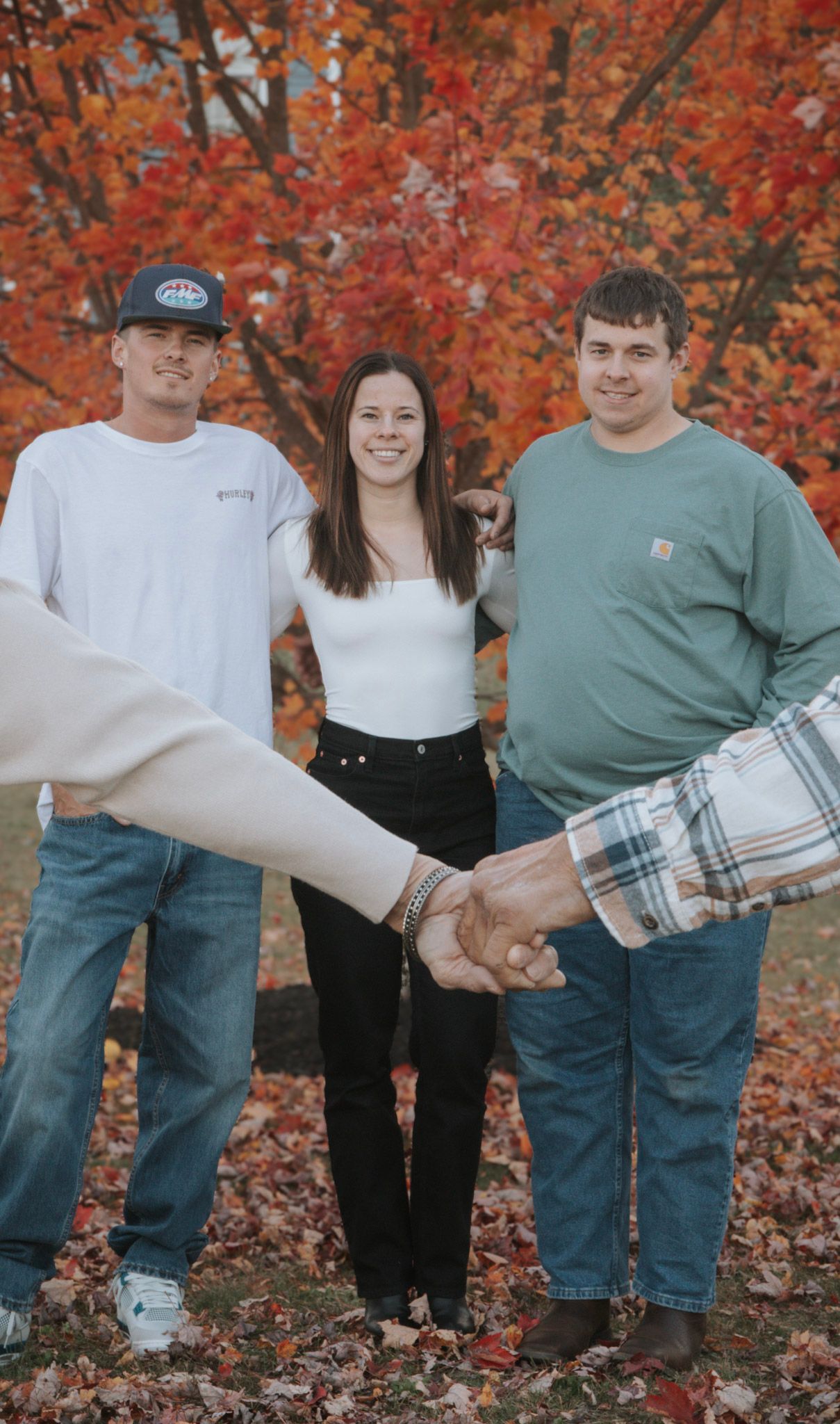 Family group photo with coordinated casual outfits against a backdrop of bright red autumn leaves.