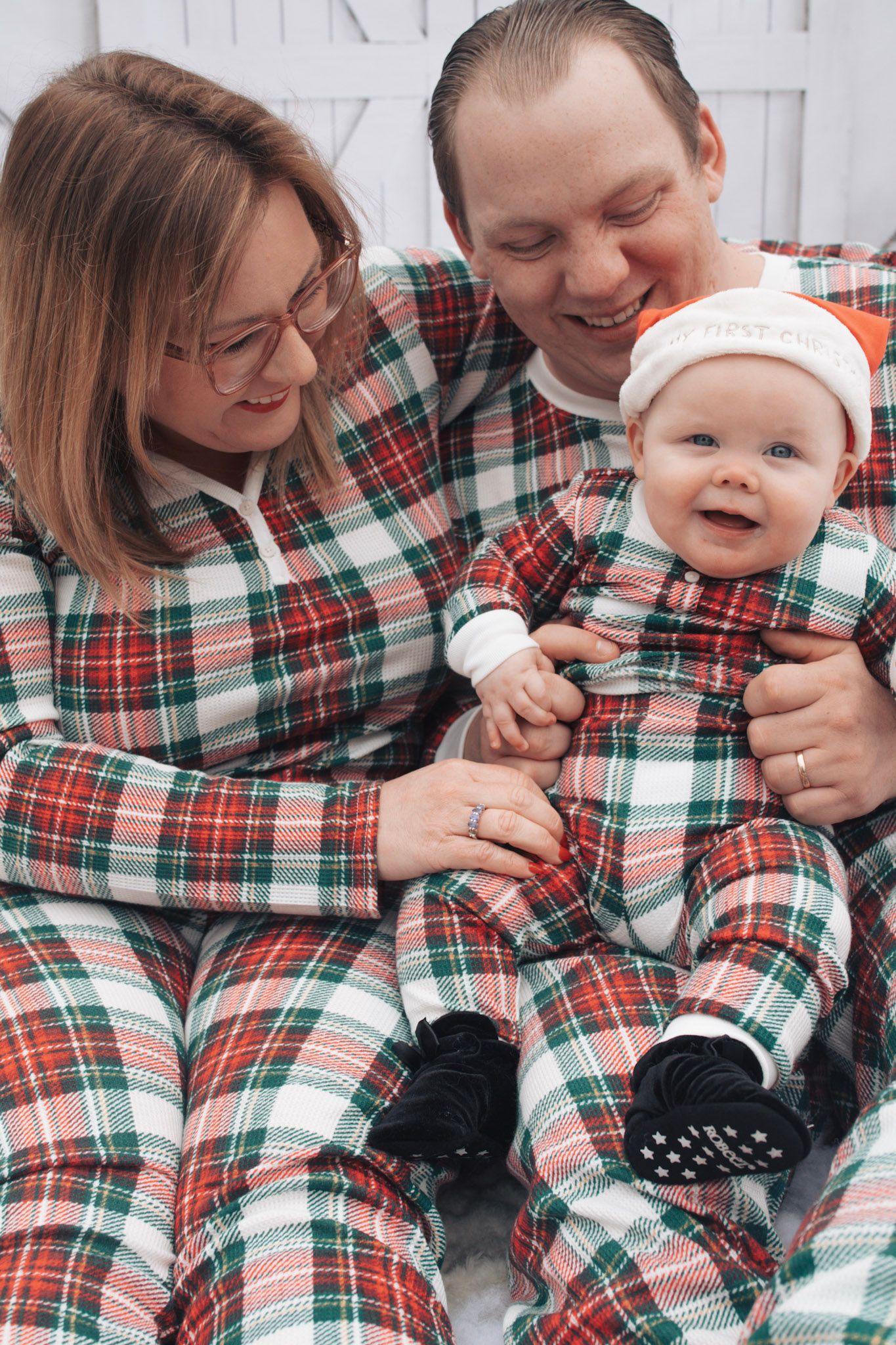 Family wearing matching plaid Christmas pajamas sharing joyful moments in winter scene.