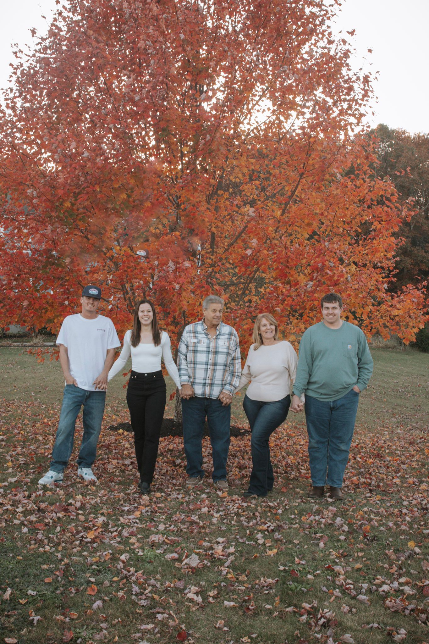 A group stands together against a backdrop of vibrant orange autumn trees with fallen leaves on the ground.