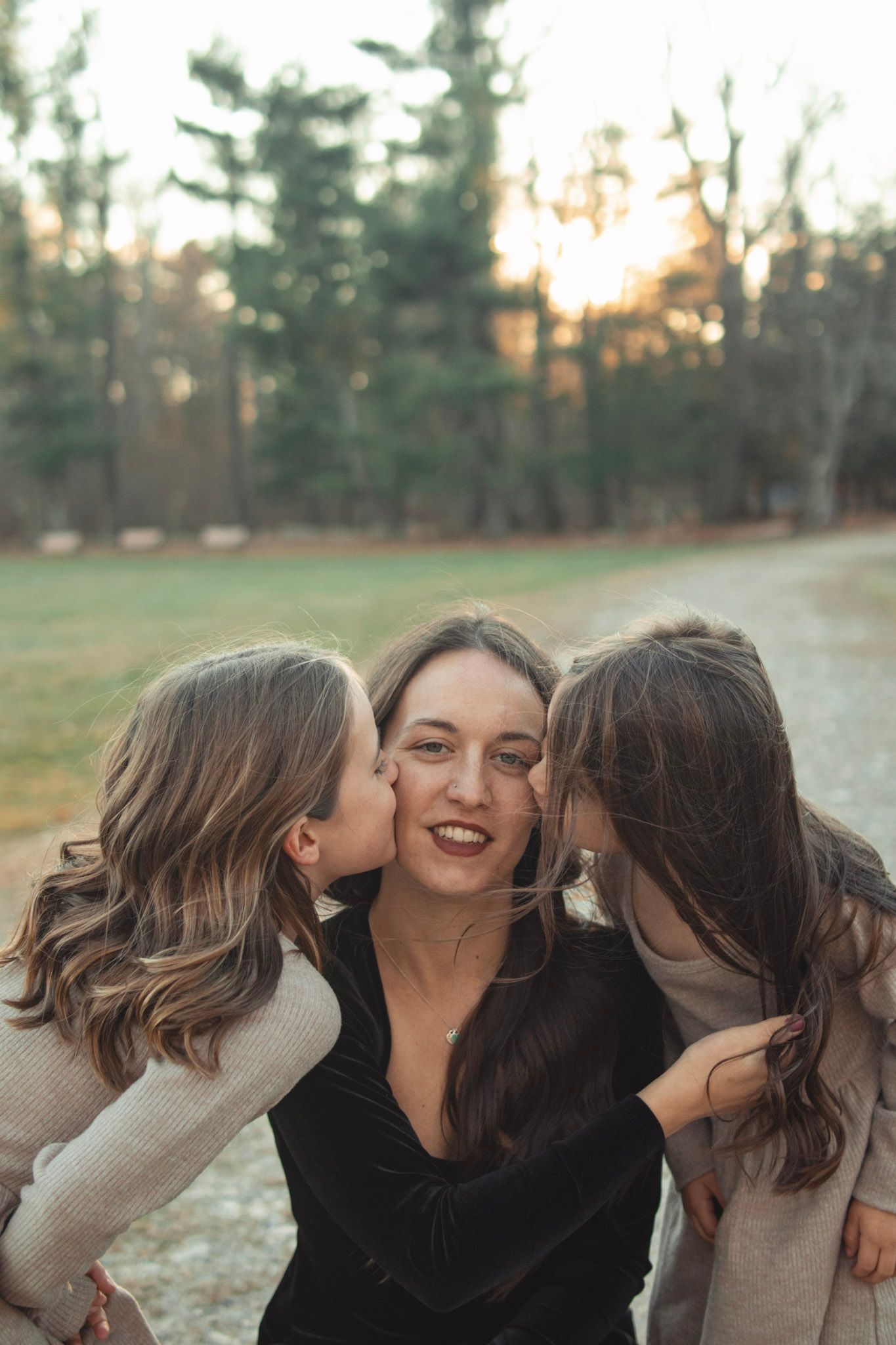 A candid moment of affection between family members sharing kisses outdoors at sunset.