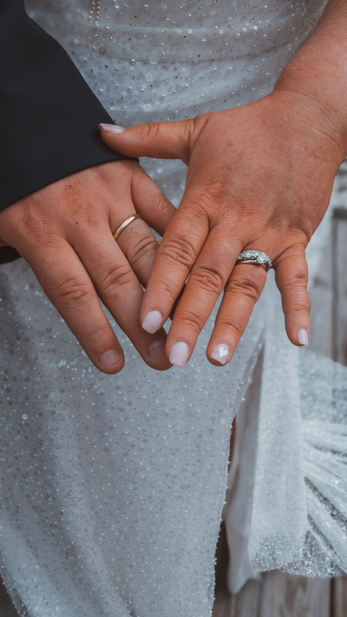 Close-up view of hands wearing a sparkling diamond engagement ring against a white lace dress background.