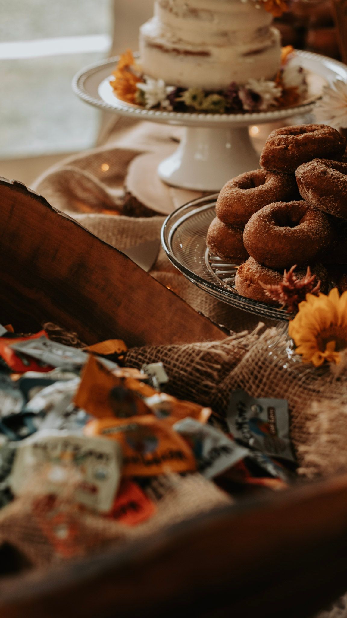 A rustic dessert table with donuts and cake decorated with autumn flowers and burlap.