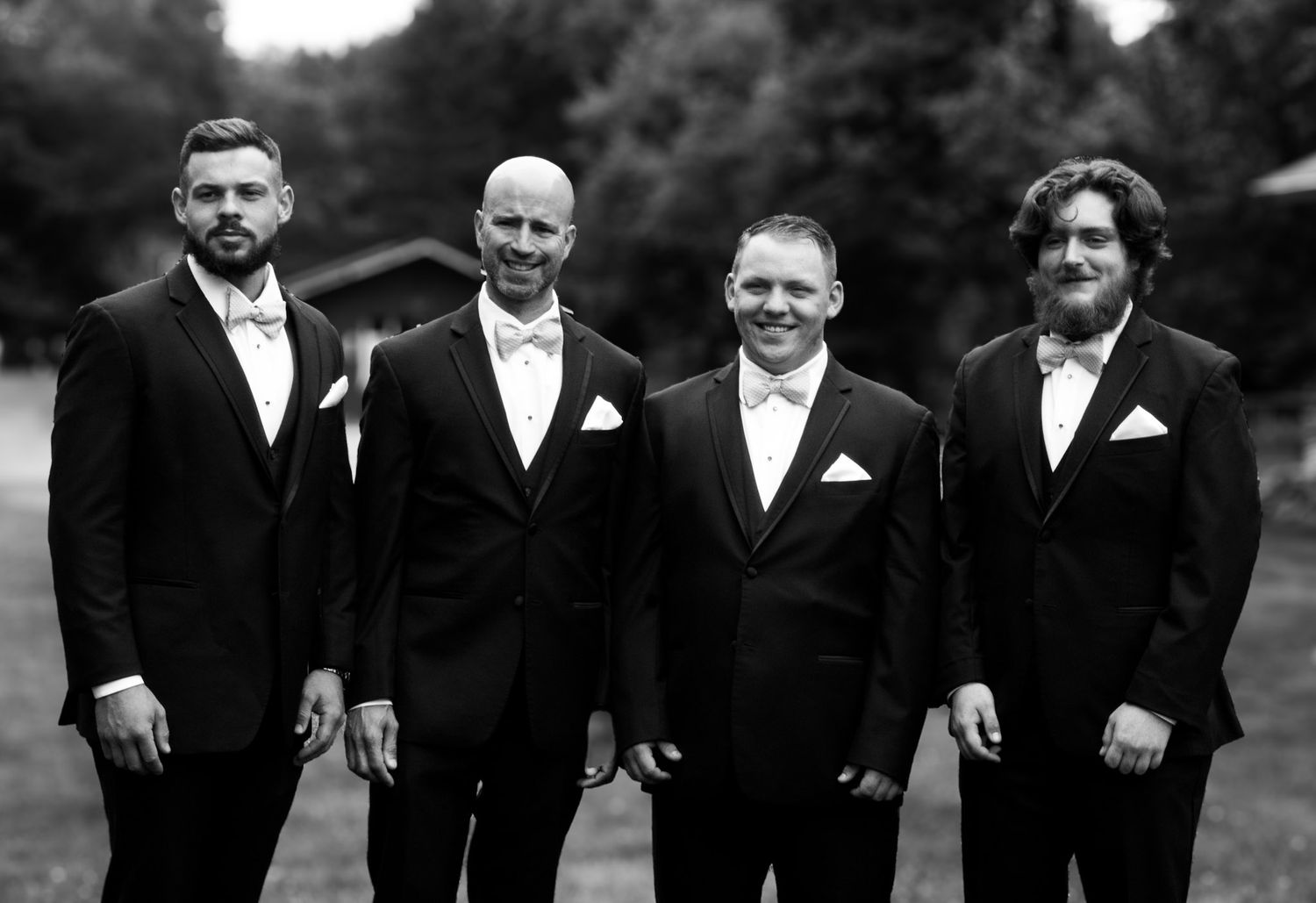Four groomsmen in formal black and white attire pose together for a classic black and white portrait.