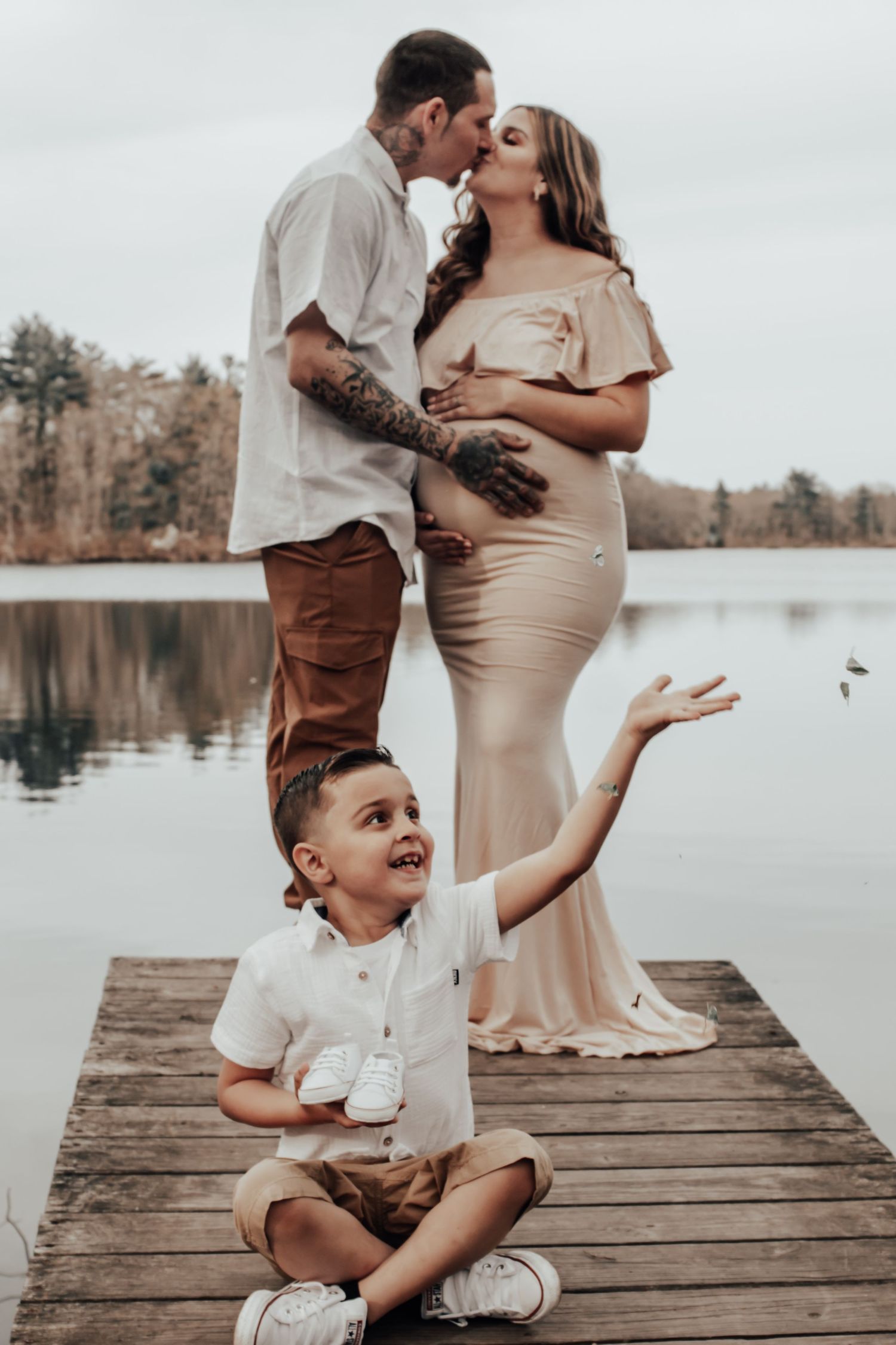 Family shares joyful moment on wooden dock during pregnancy photoshoot by lake.