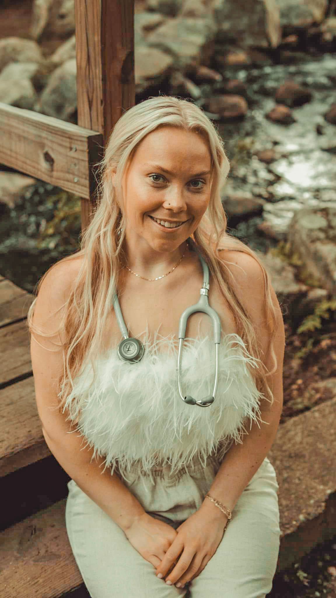 A person in a light-colored feathered top poses outdoors in a natural setting.