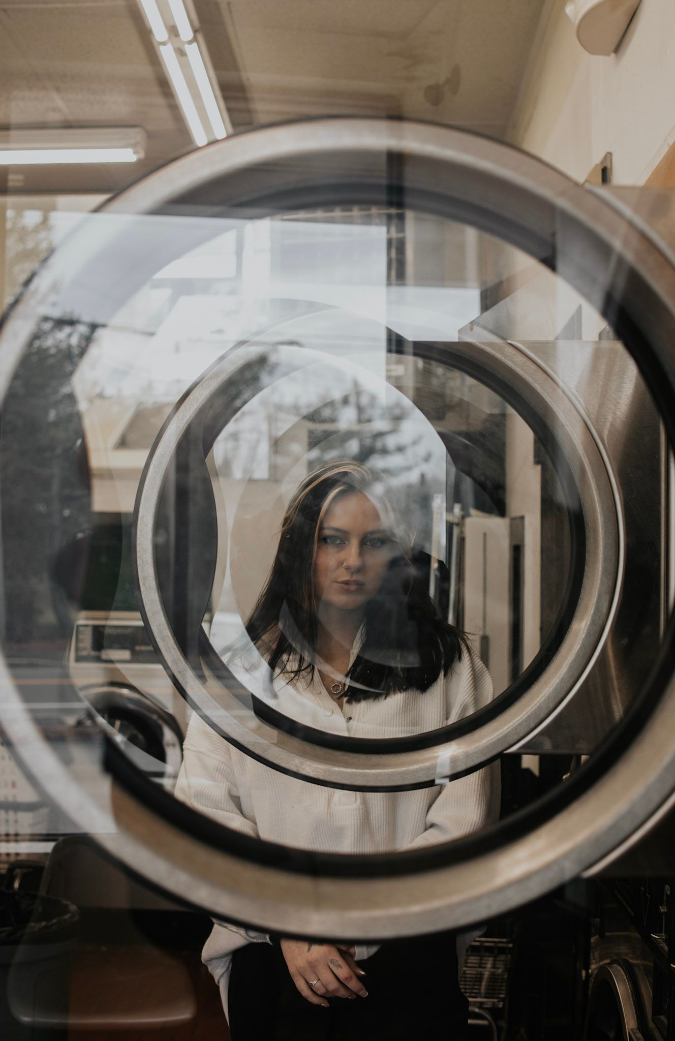 View through circular washing machine door window showing reflective glass and laundromat interior.