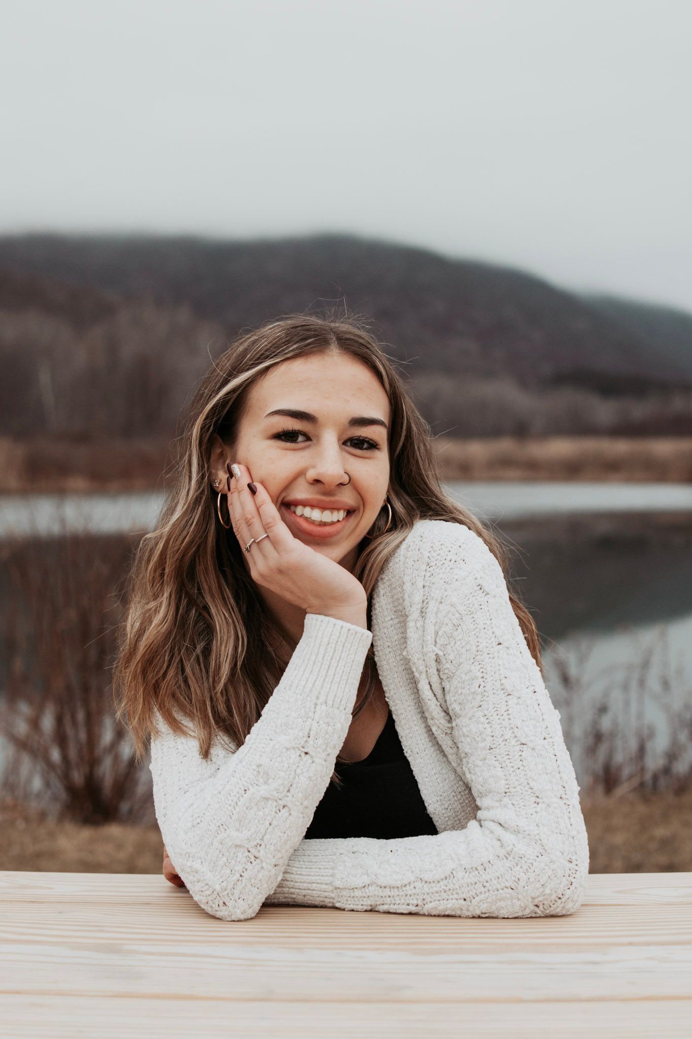 Person in white sweater lying on wooden surface with winter lake and mountains in background.