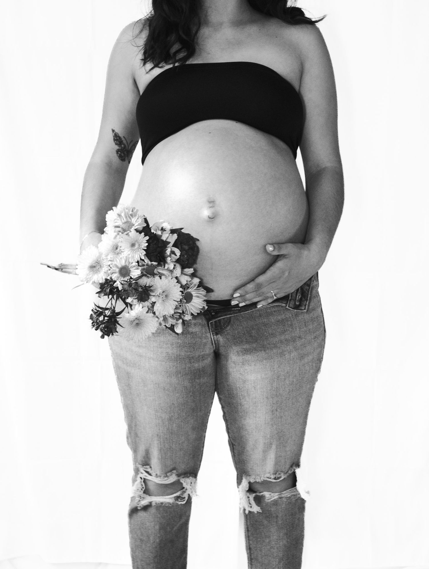 Three black and white photos showing pregnant bellies with flowers arranged artistically on the bare skin.